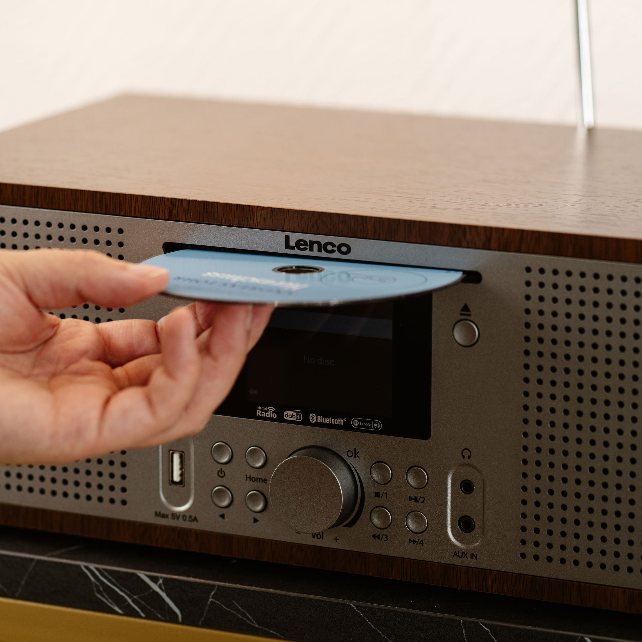 Una mano inserisce un CD blu in una radio Lenco con pannello frontale argentato.