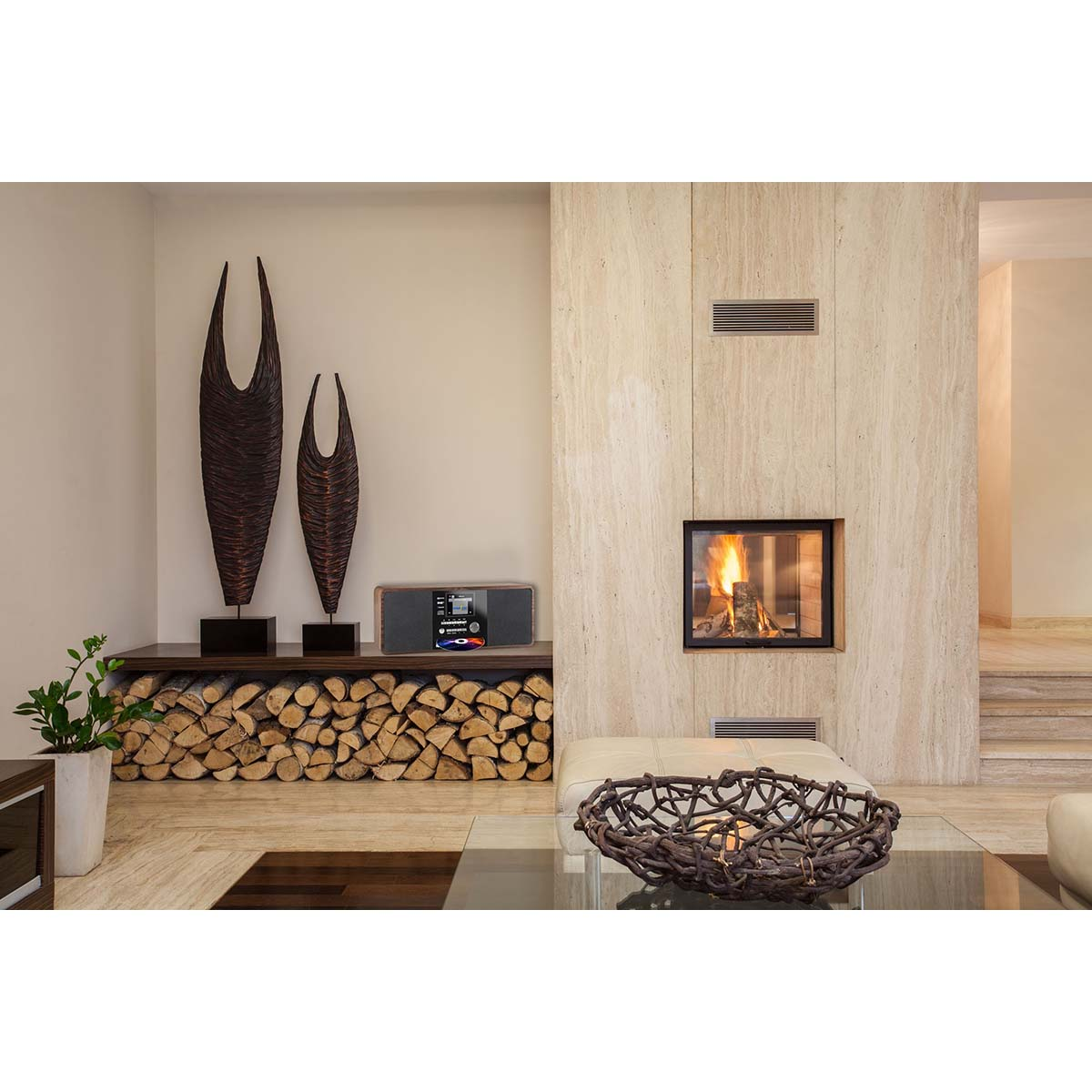 Ein Wohnzimmer mit Kamin, Holzstapel, zwei Skulpturen und einem Radio.