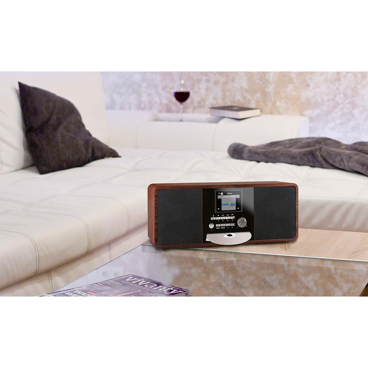 Ein Holzradio mit CD-Schlitz steht auf einem Glastisch vor einem weißen Sofa.