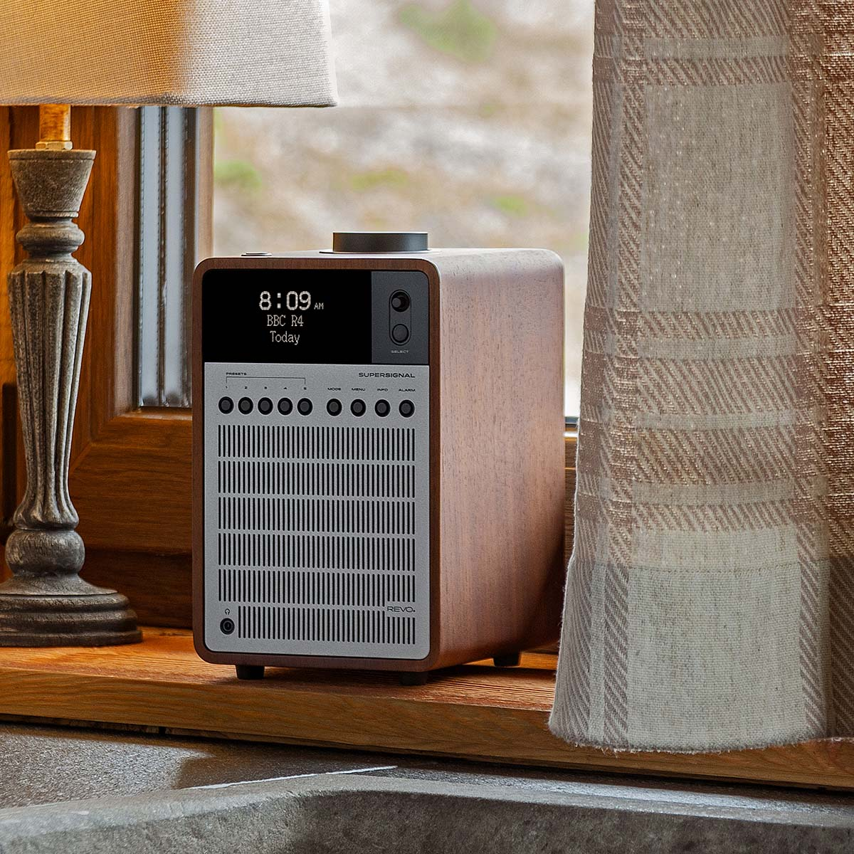 Een houten radio met display en knoppen staat op een vensterbank bij een raam.