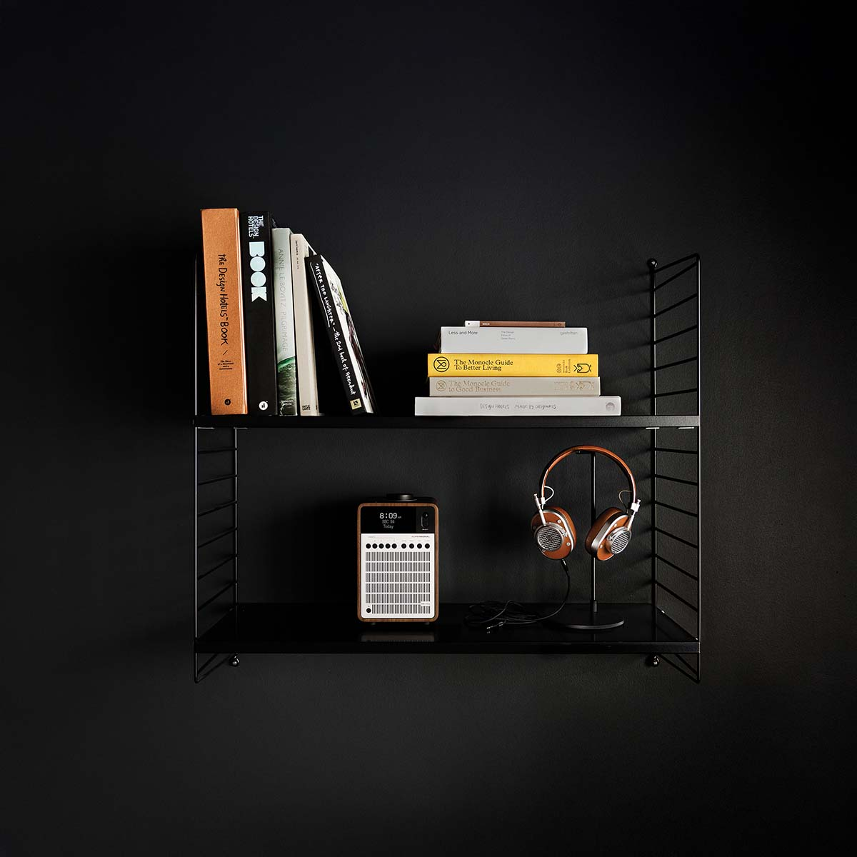 Twee planken met boeken, een radio en koptelefoon op zwarte achtergrond.