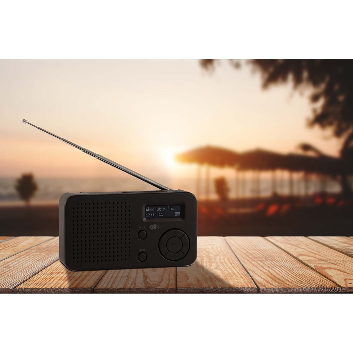 Radio noire avec antenne déployée sur table en bois, plage en arrière-plan au coucher du soleil.