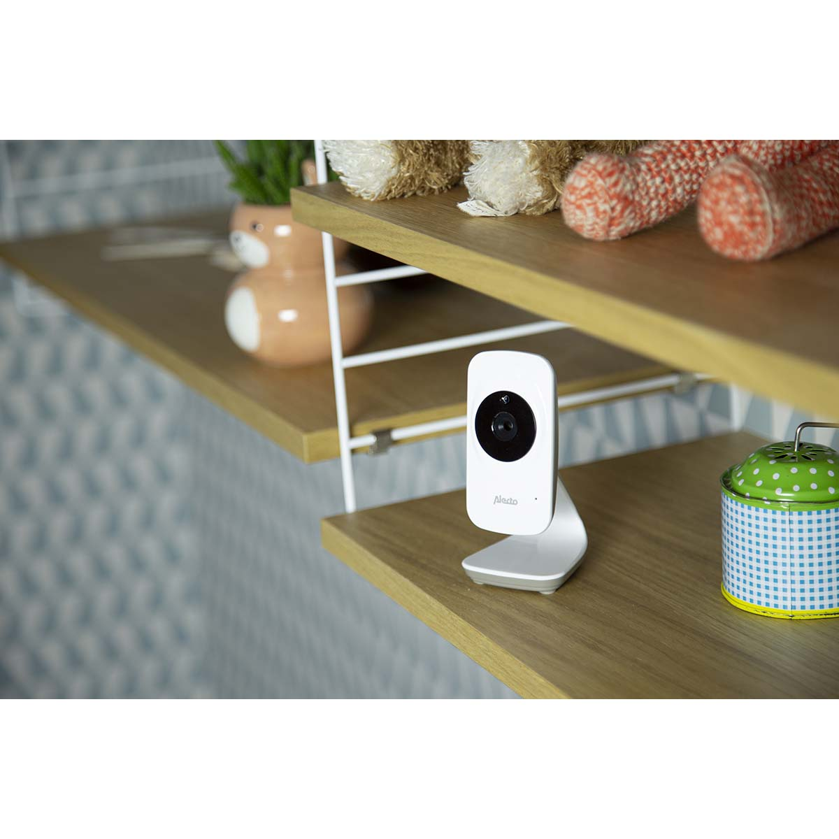 Ein weißer Babyfon-Monitor steht auf einem Holzregal neben Stofftieren und einer grünen Dose.