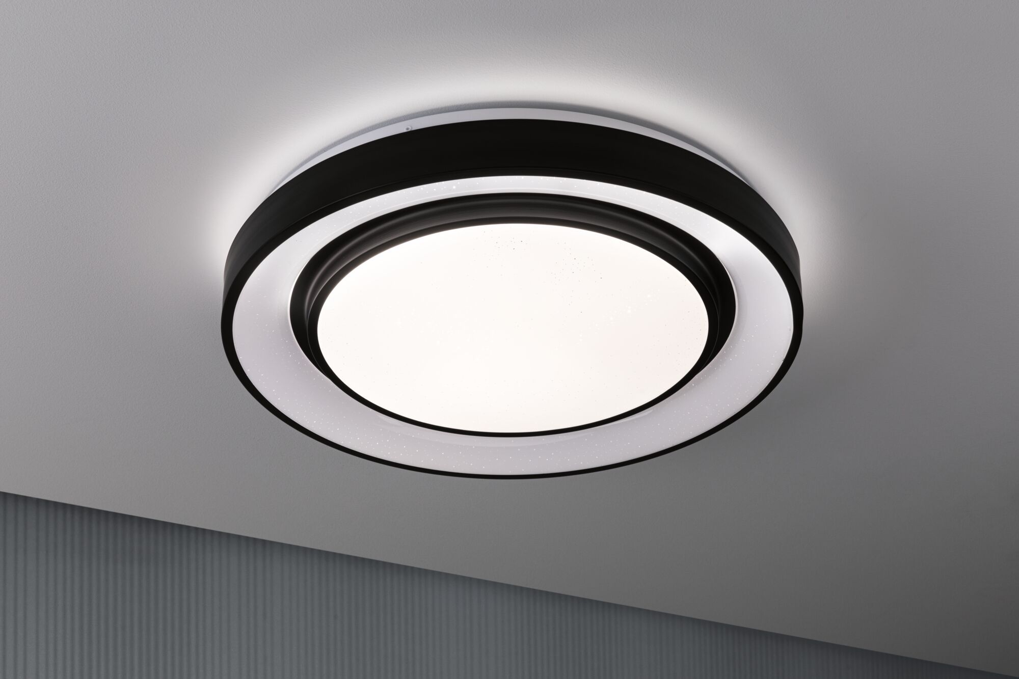 Plafoniera rotonda con cornice bianca e nera, illuminata.