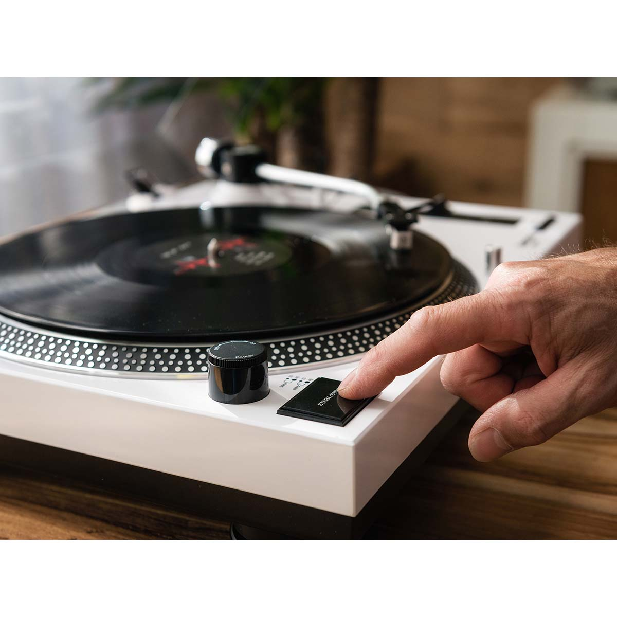 Un dedo presiona el botón de inicio/parada de un tocadiscos blanco.