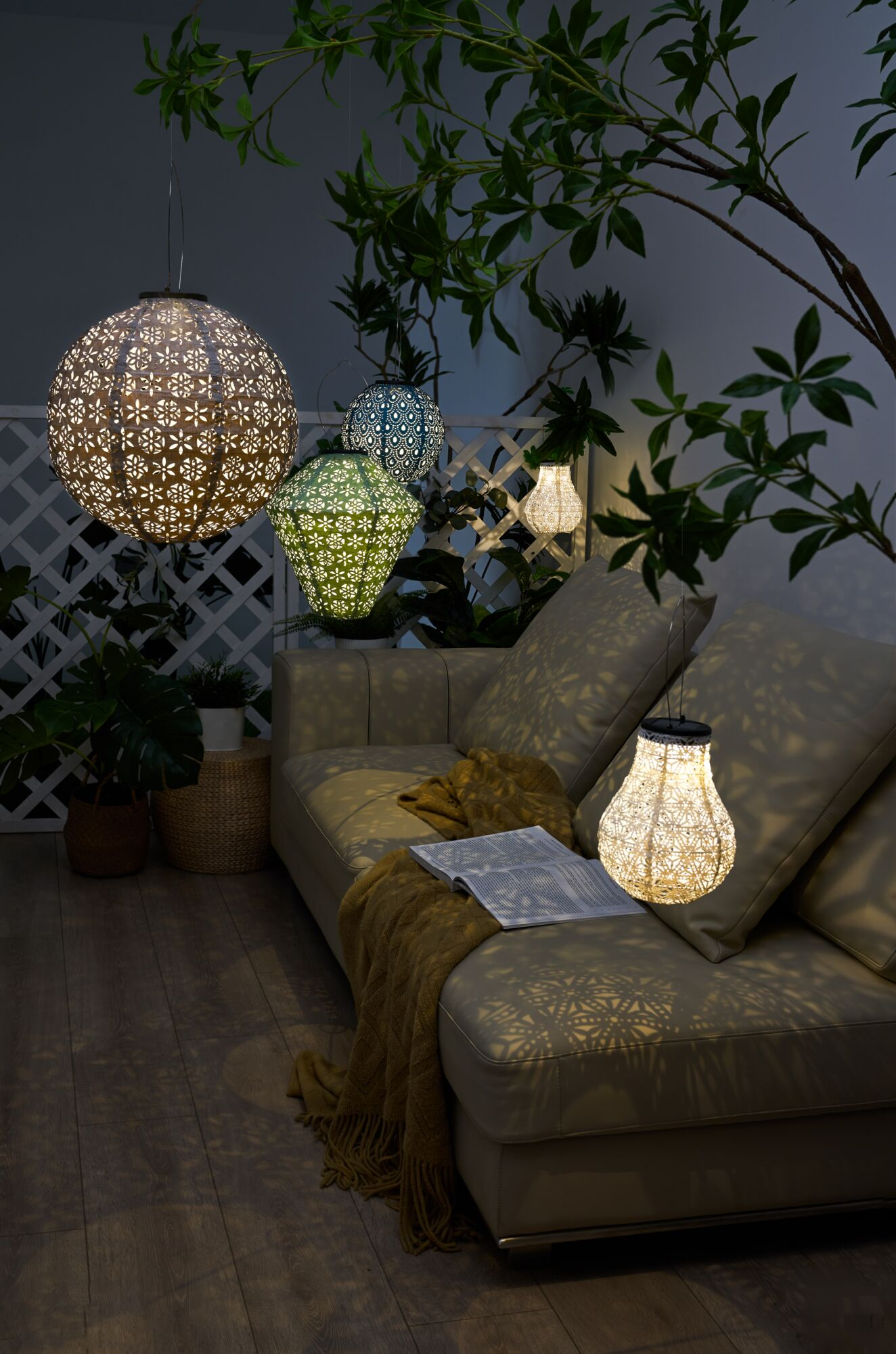 Wiszące lampiony oświetlają zewnętrzną kanapę z poduszkami i kocem.