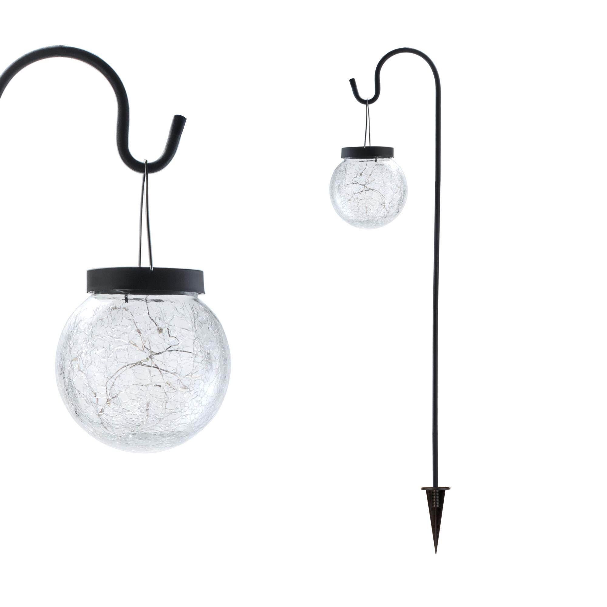 Dwa czarne metalowe haczyki trzymające szklane latarnie, jedna ze sznurkiem i szpilką.