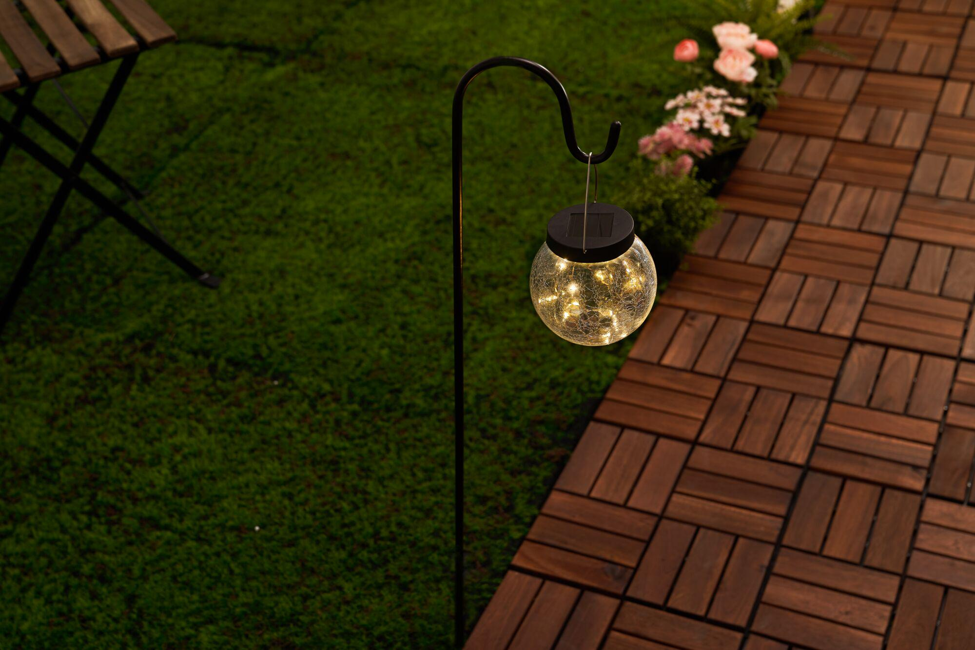 Solarna latarnia wisząca ze światłami na haku nad drewnianym patio.