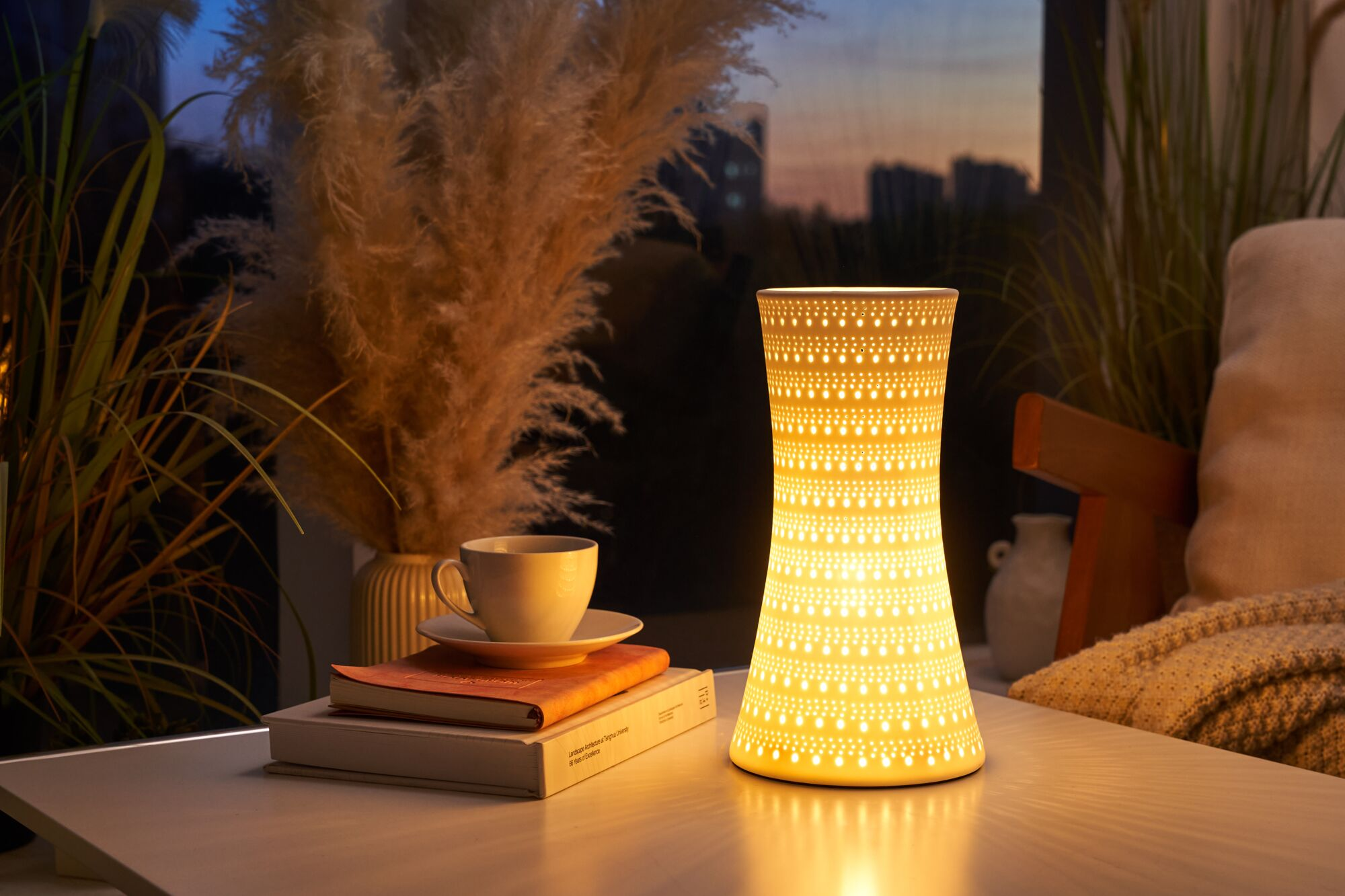 Podświetlana lampa obok książek i filiżanki herbaty, z roślinami w tle.