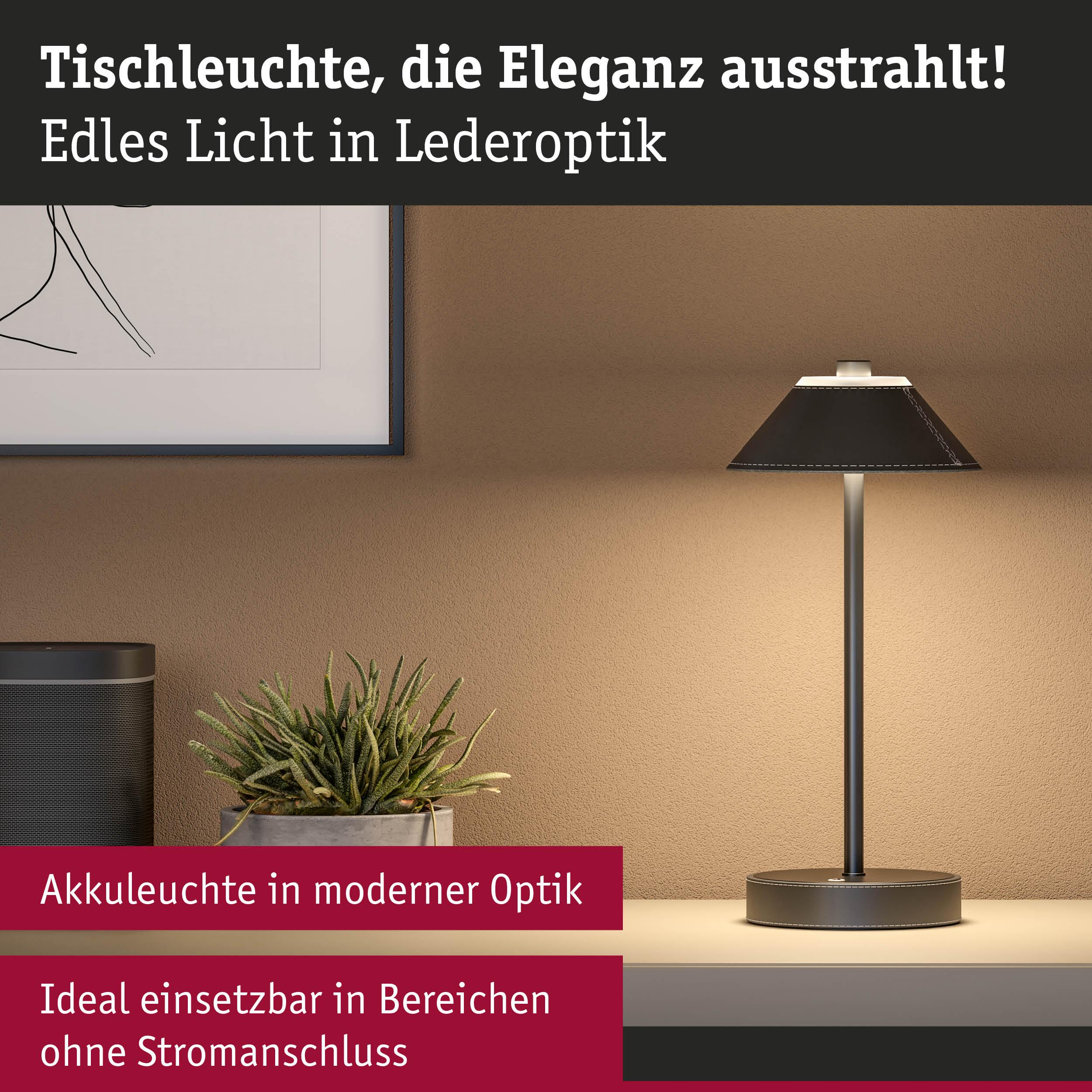 Czarna lampa stołowa w optyce skóry z przeszyciami, obok rośliny i głośnika.