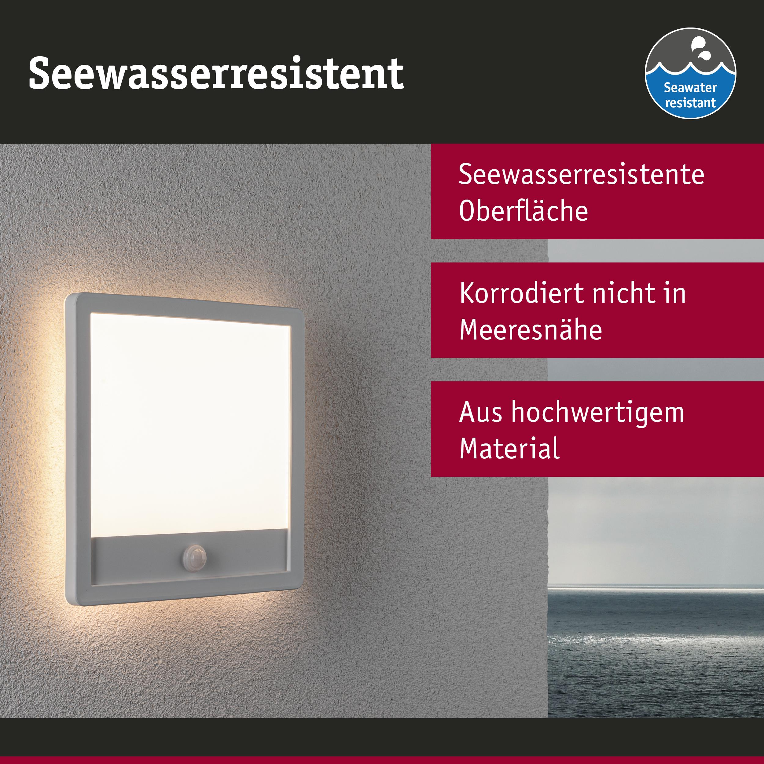 Eine weiße Wandleuchte mit Bewegungsmelder an einer strukturierten Wand über dem Meer.