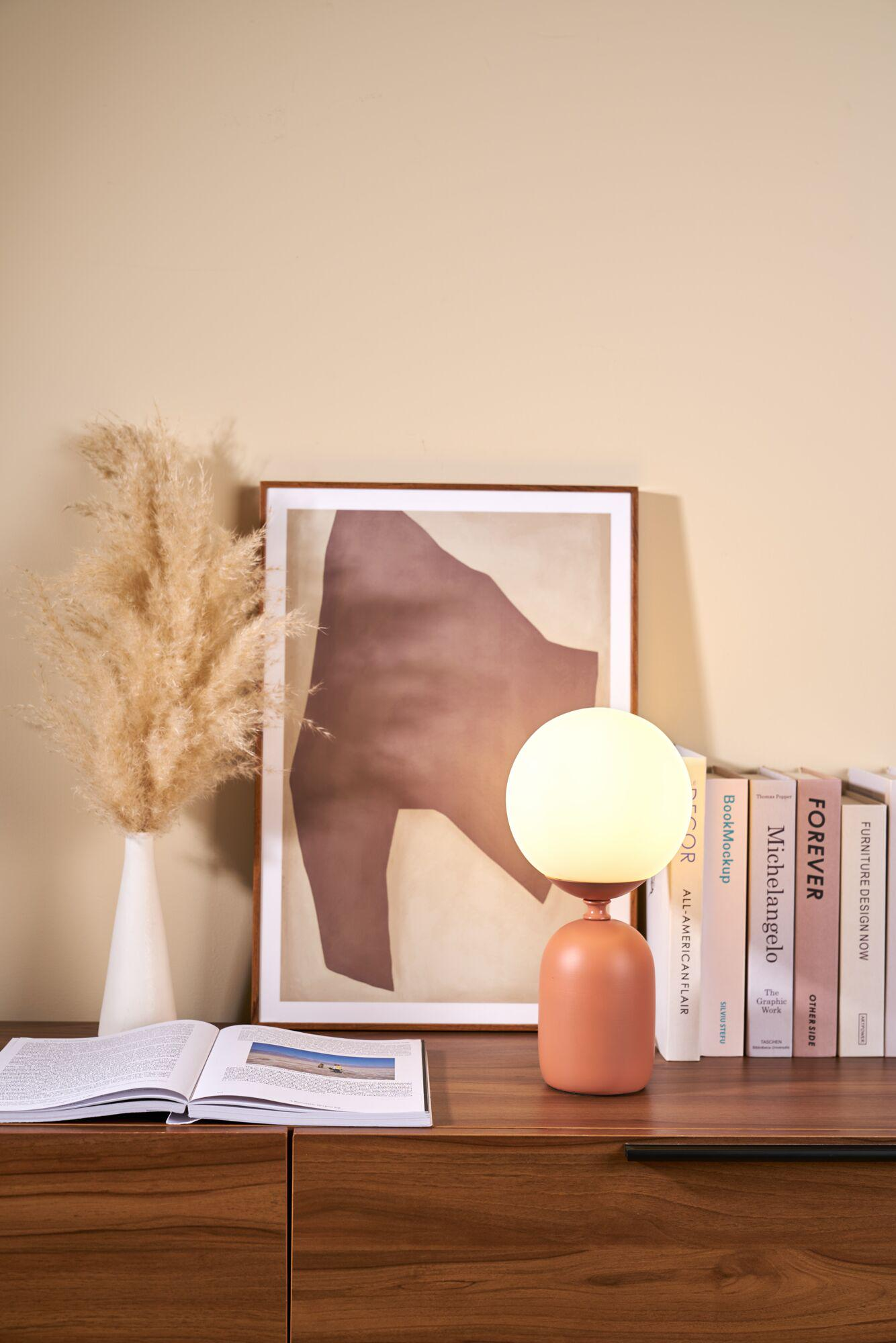 Pomarańczowa podstawa lampy z okrągłą białą szklaną lampą stoi obok książek.