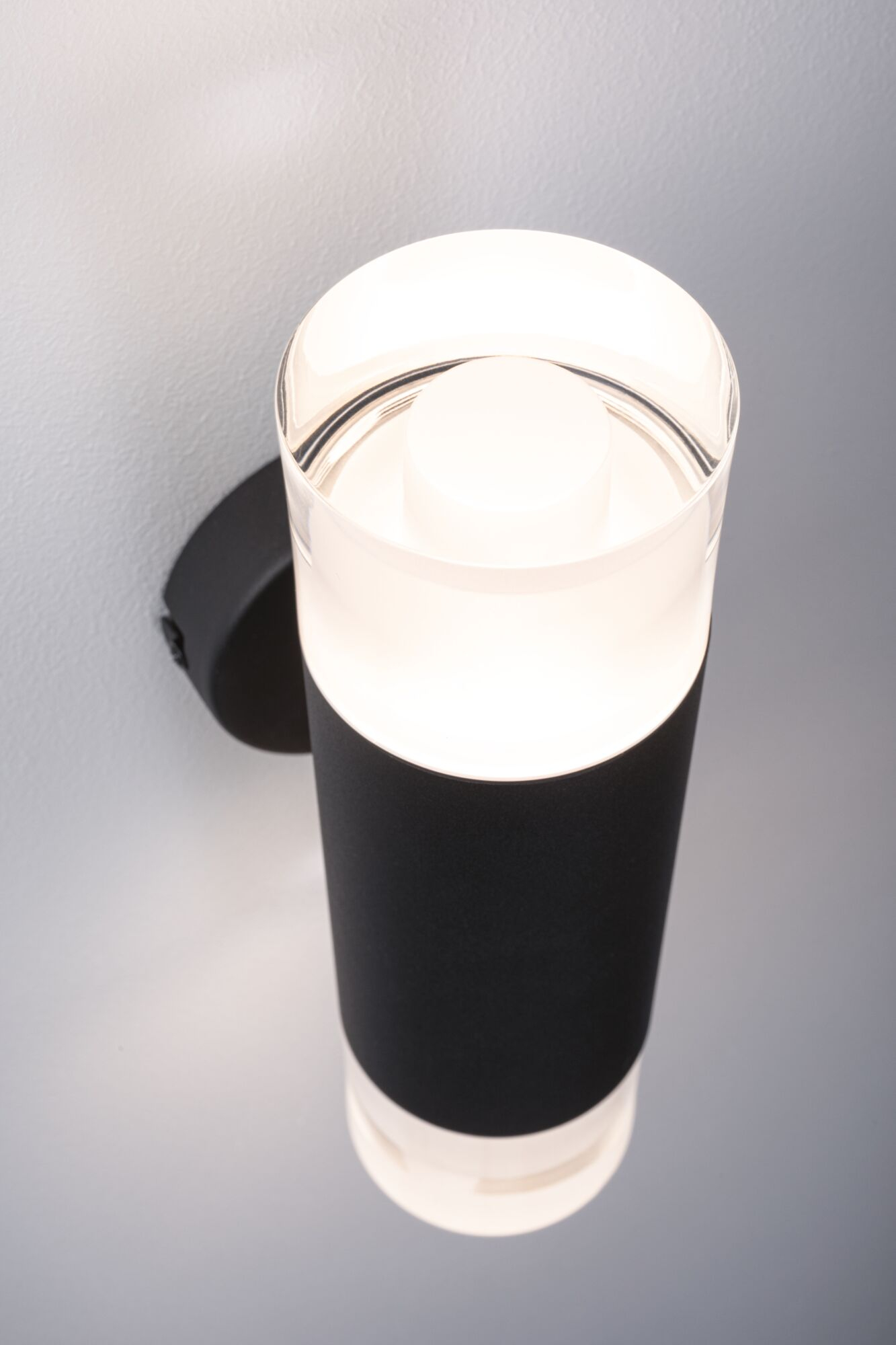 Eine moderne schwarze und klare zylindrische Wandleuchte aus Glas ist an einer grauen Wand montiert.