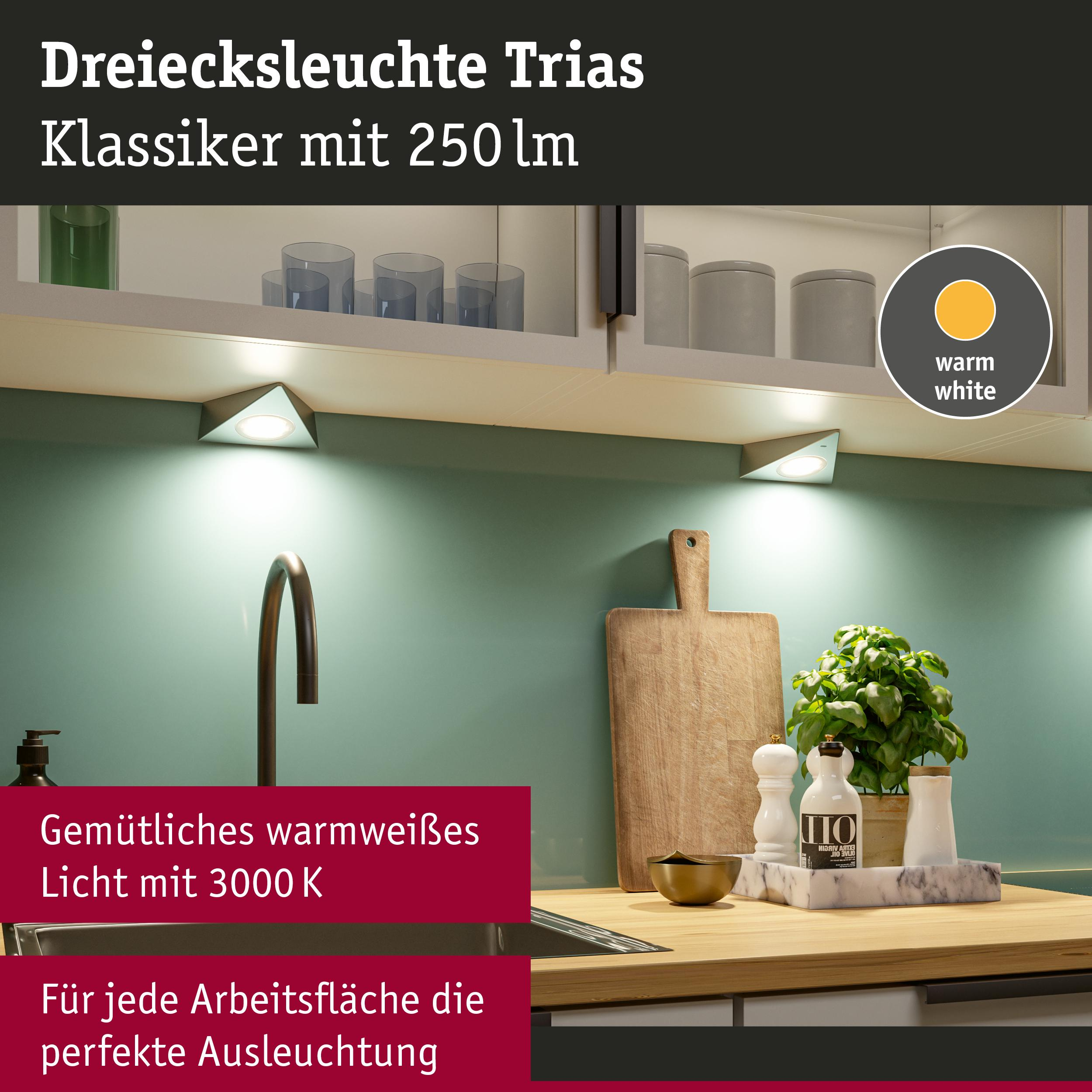 Trójkątna lampa Trias z ciepłym białym światłem nad blatem.