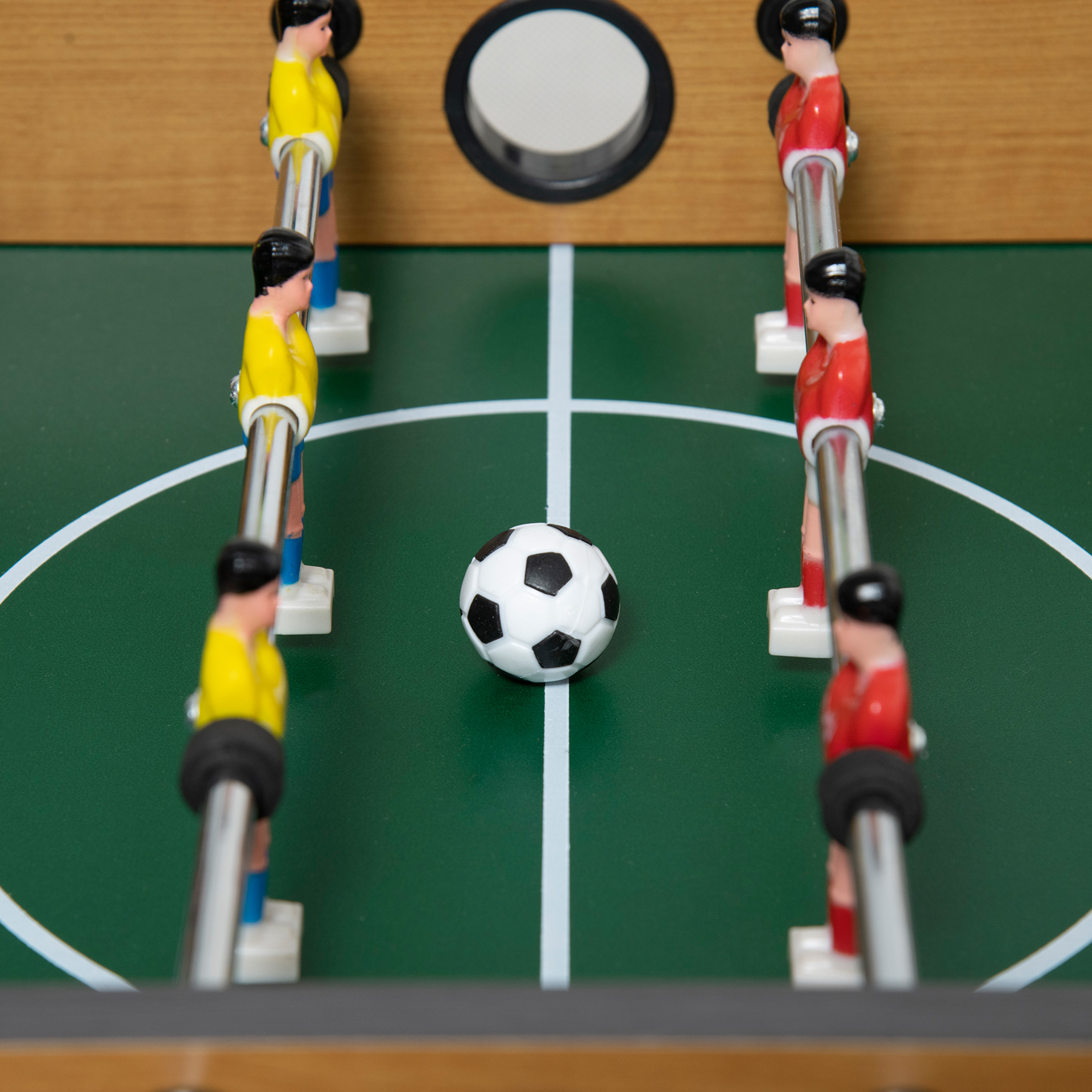 Campo de futbolín con balón y figuras de jugadores en rojo y amarillo.