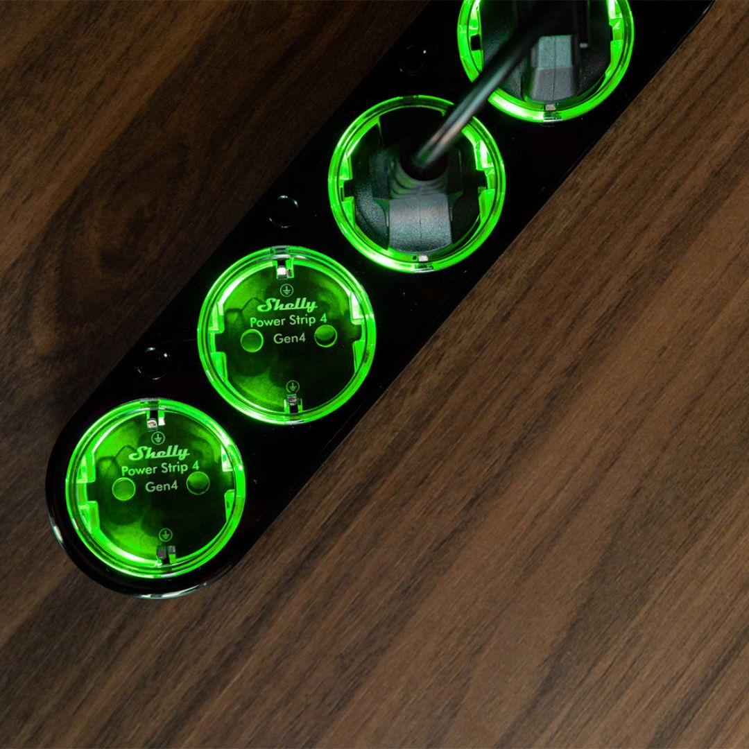 Czarna listwa zasilająca Shelly Power Strip 4 Gen 4 z zielonym podświetleniem na drewnianym stole.