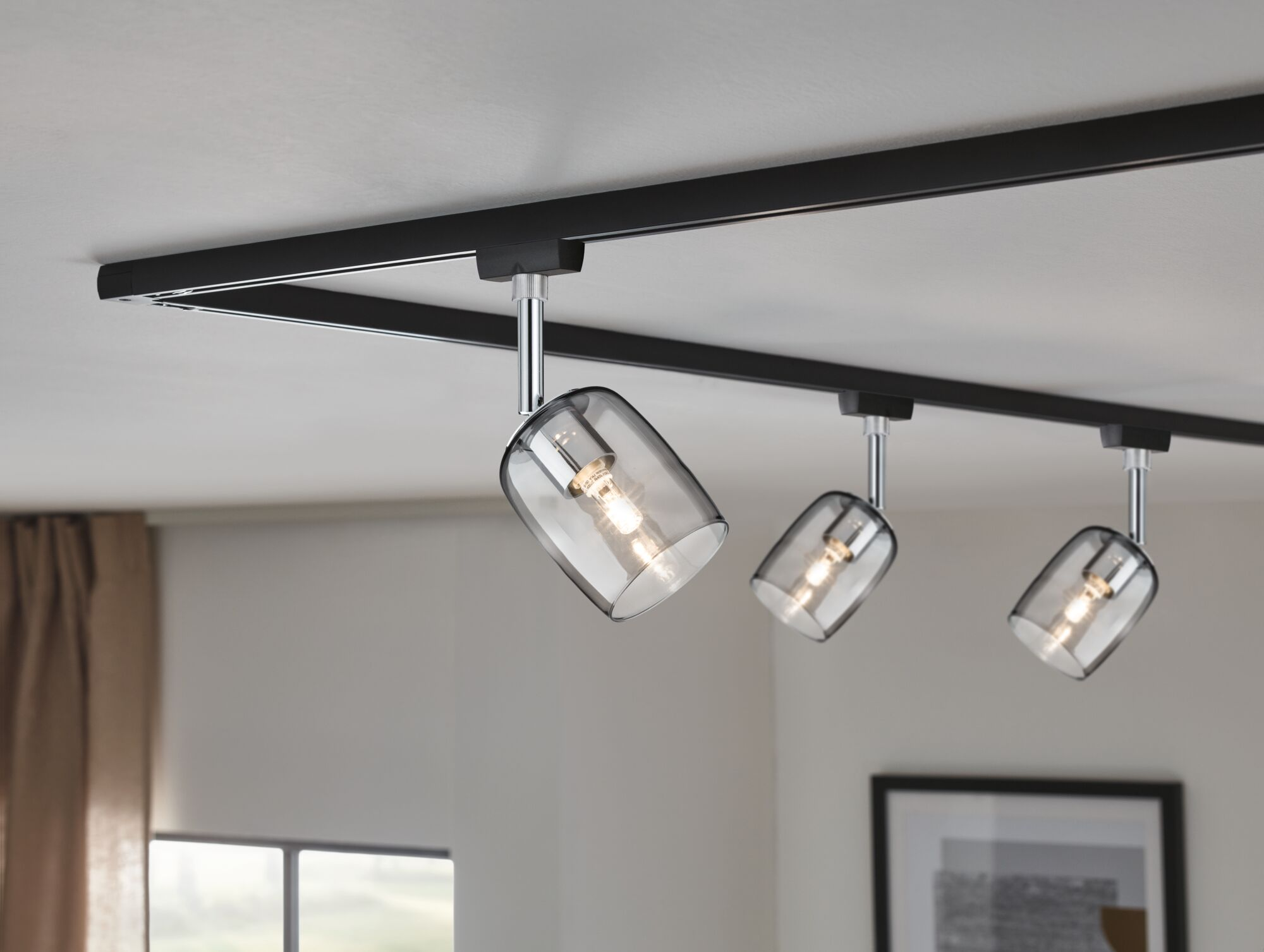 Eine schwarze Schienenleuchte mit drei Glasschirmen an einer weißen Decke.