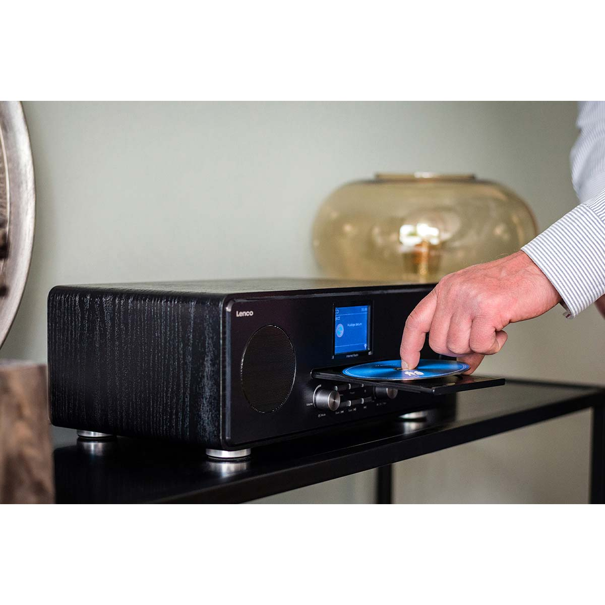 A hand inserts a CD into a black Lenco stereo with a blue screen and speaker.