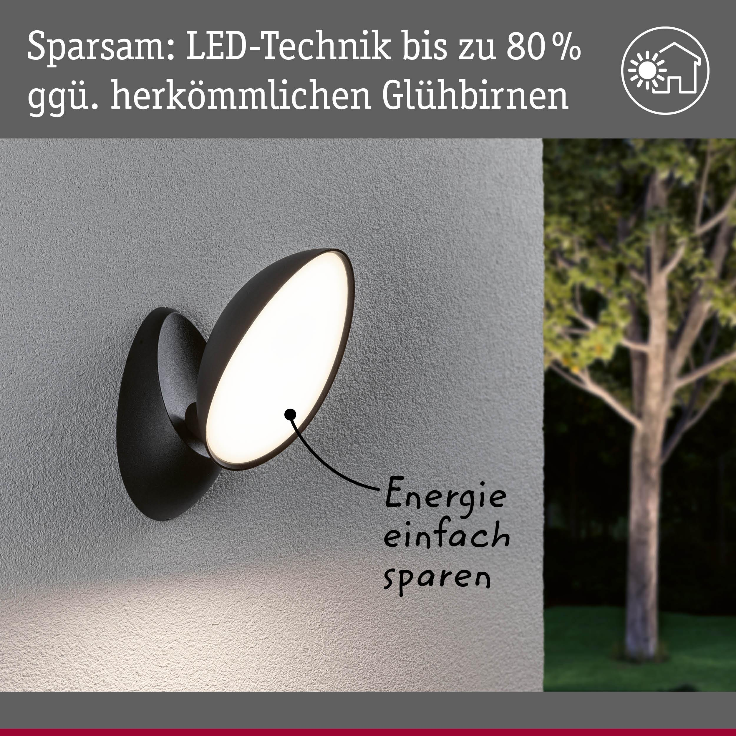 Czarna lampa ścienna z technologią LED, obok drzewa w ogrodzie.