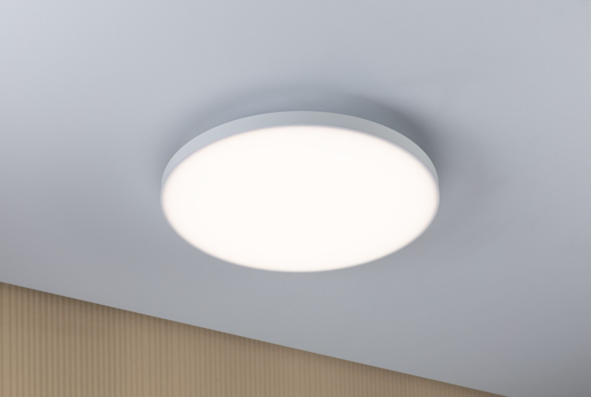 Eine runde, weiße Deckenleuchte mit hellem Licht auf einer grauen Decke.