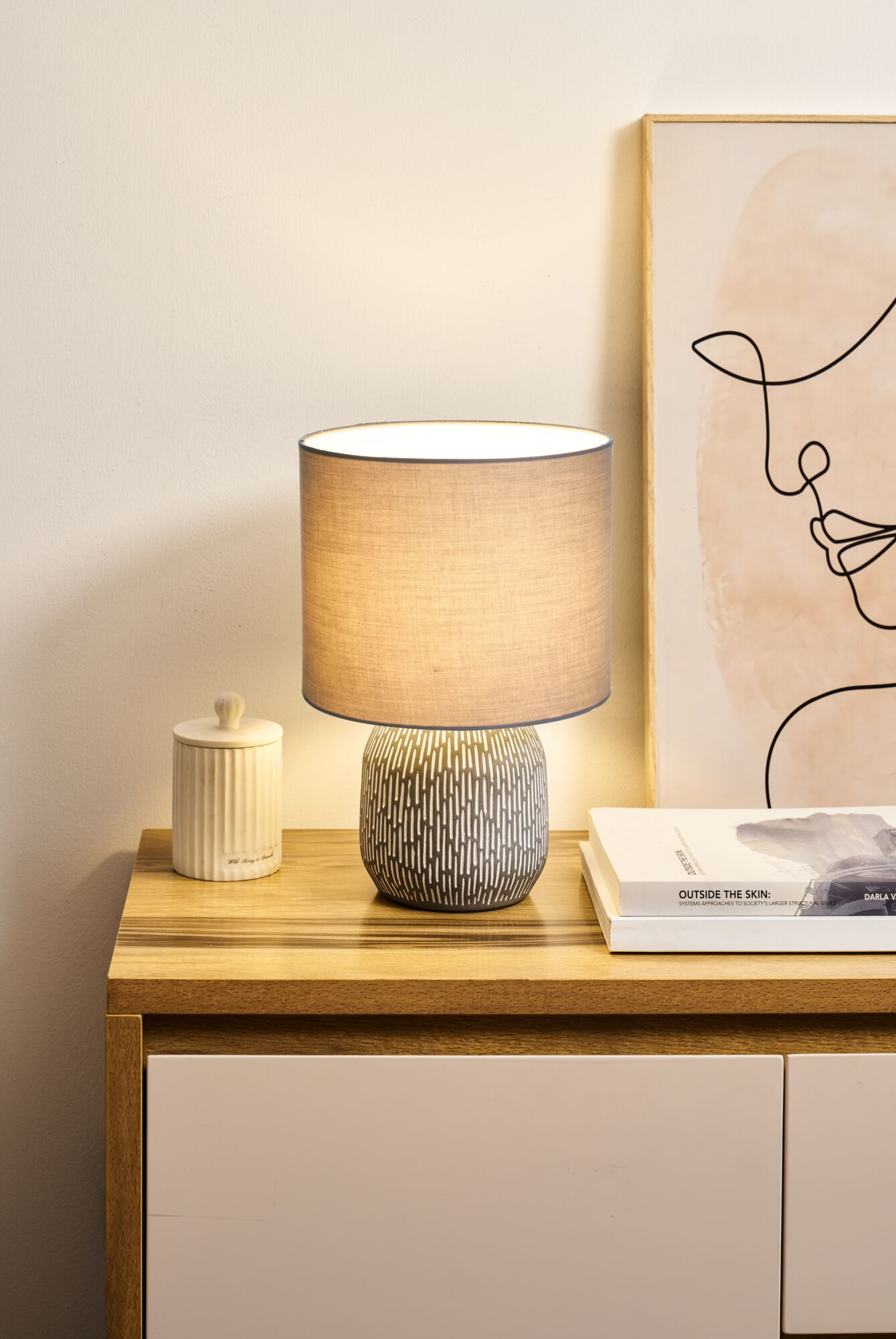 Wzorzysta lampa stoi na szafce nocnej obok ceramicznego słoika i książek.