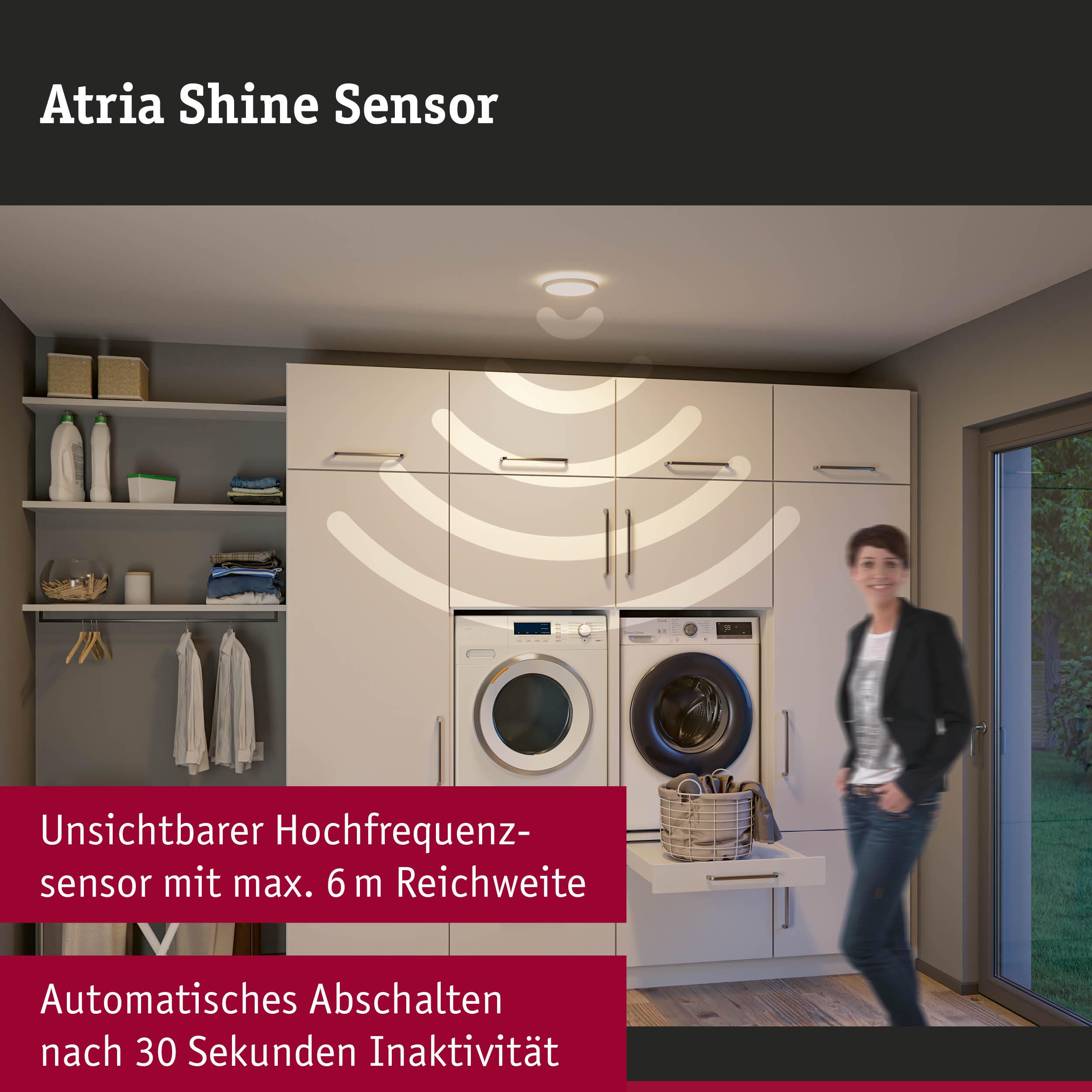 Eine Frau steht in einem Waschraum neben Waschmaschinen. Ein Sensor ist an der Decke.