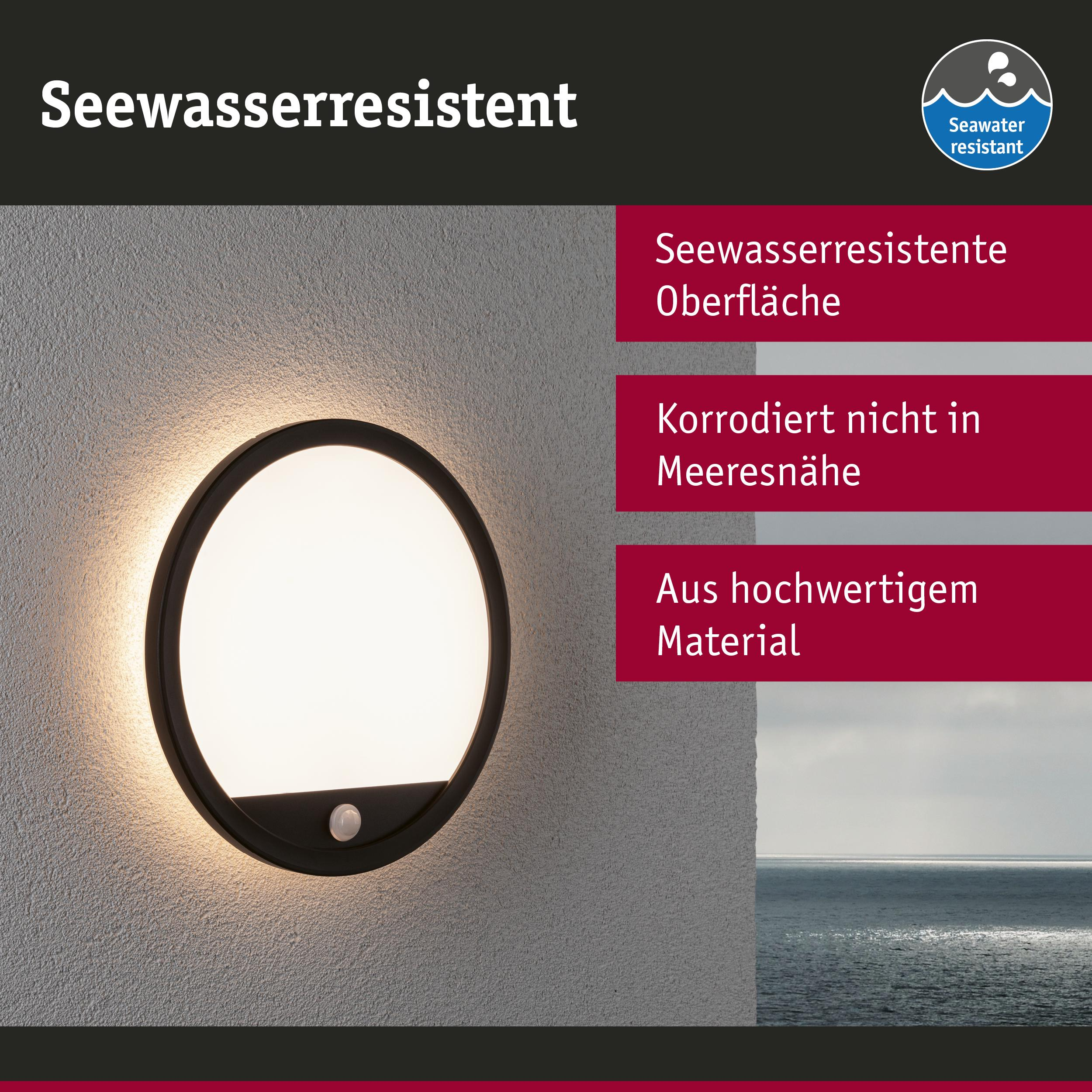 Eine runde, schwarze Außenleuchte mit Bewegungsmelder an einer Wand, daneben das Meer.