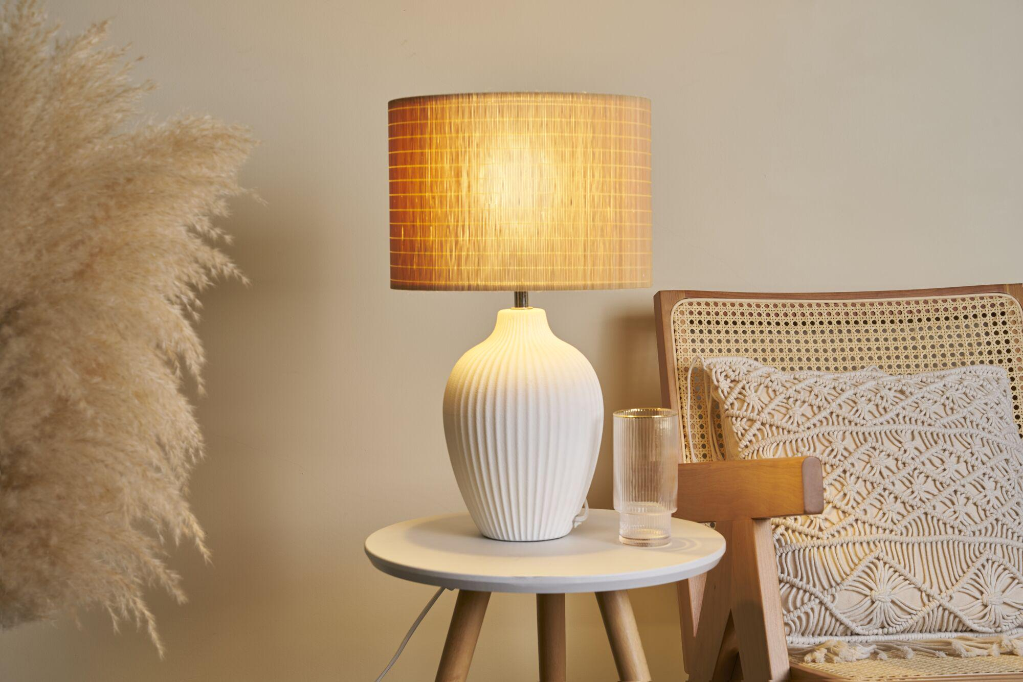 Biały stolik nocny z lampą, szklanką i dużą trawą pampasową.