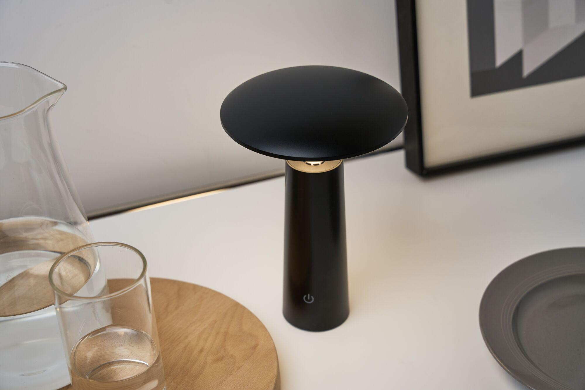 Czarna lampa stoi na stole obok szklanego dzbanka i talerza.