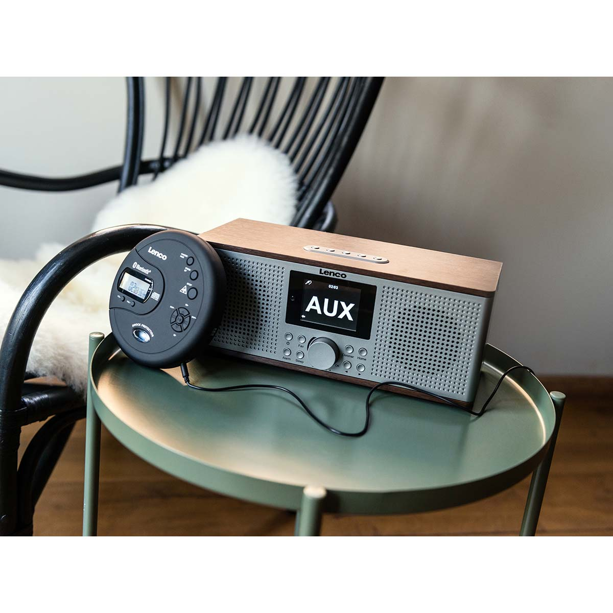Odtwarzacz CD Lenco i drewniane radio stoją na okrągłym zielonym stole obok krzesła.