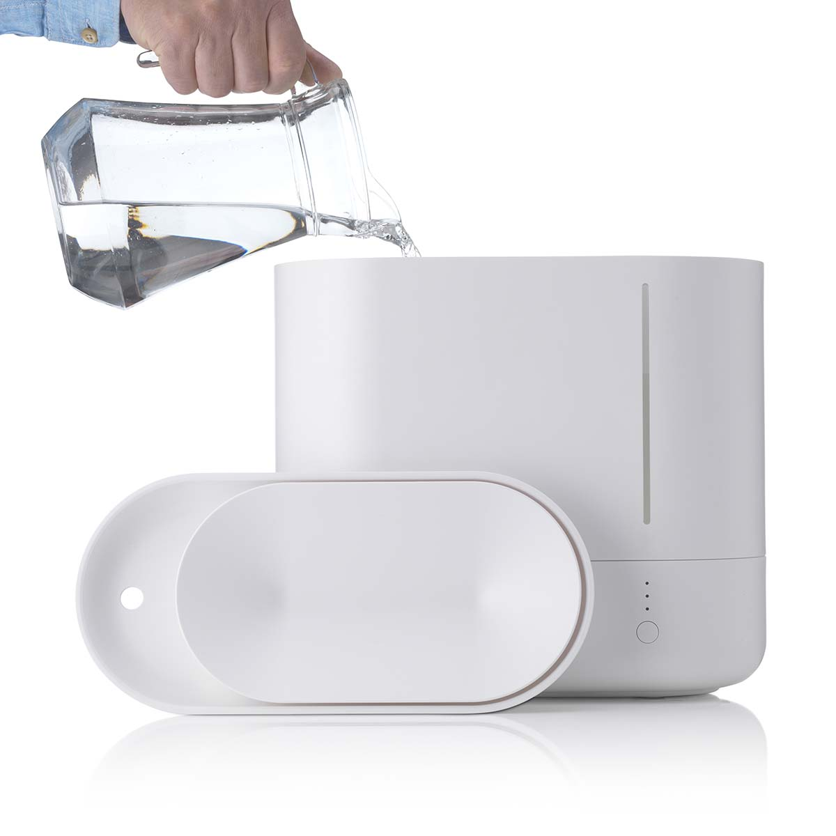 Eine Hand gießt Wasser aus einem Glasbehälter in einen weißen Luftbefeuchter.