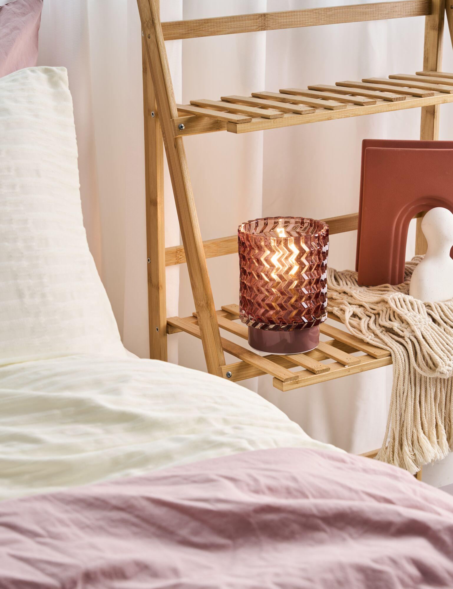 Podświetlany świecznik na drewnianej półce obok łóżka.