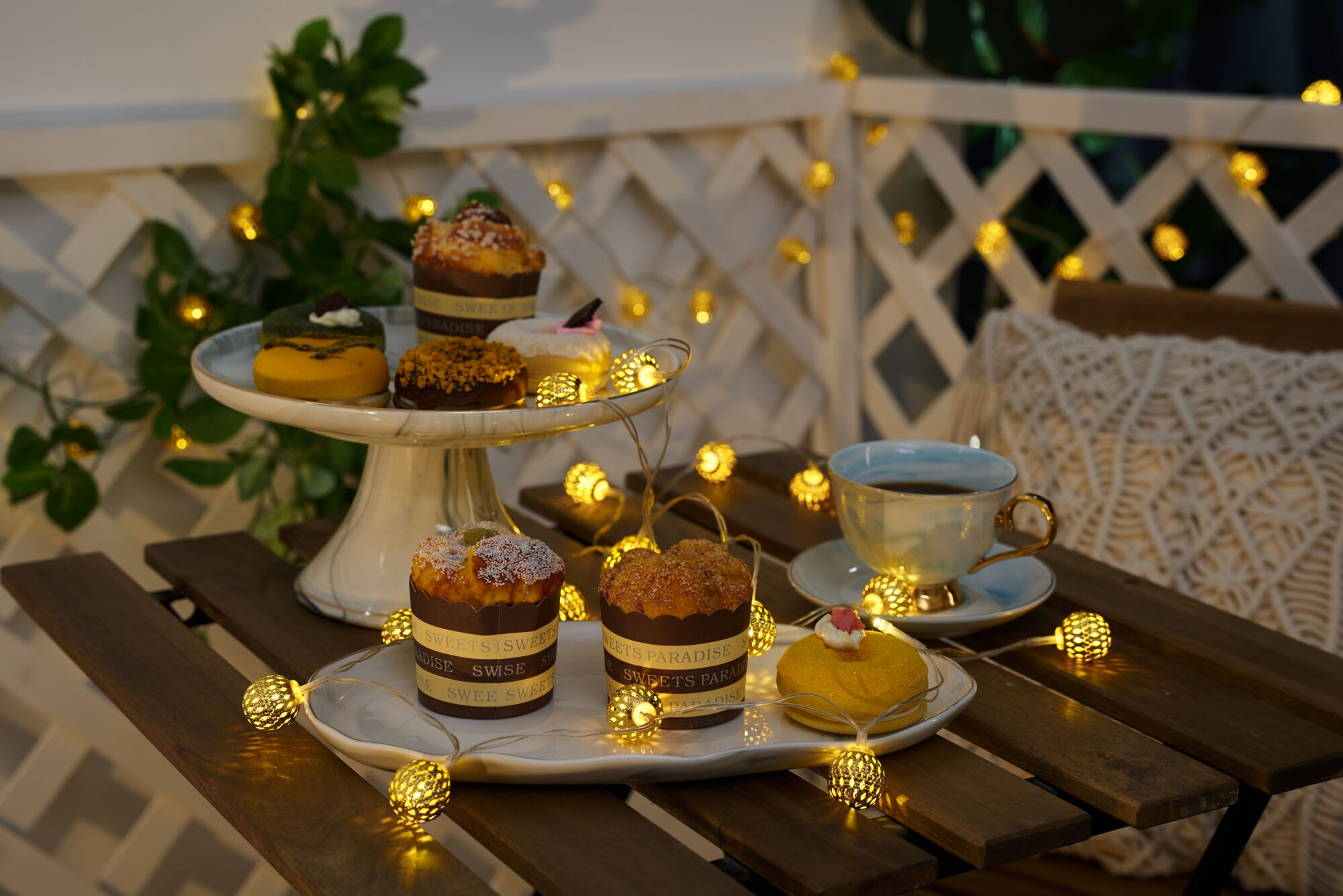 Desery i filiżanka herbaty na drewnianym stole, oświetlone lampkami.