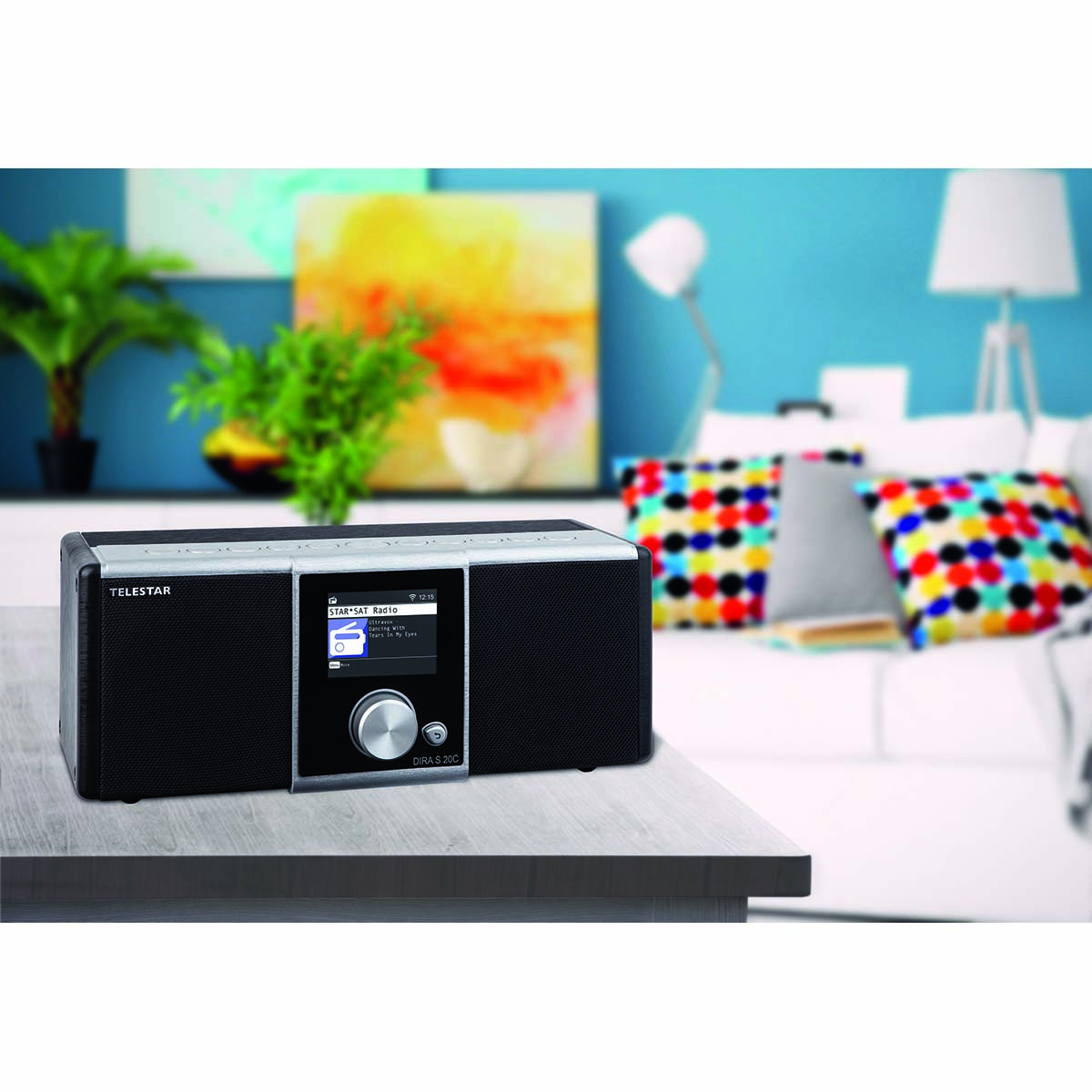 A black Telestar DAB+ radio sits on a wooden table. Living room in background.