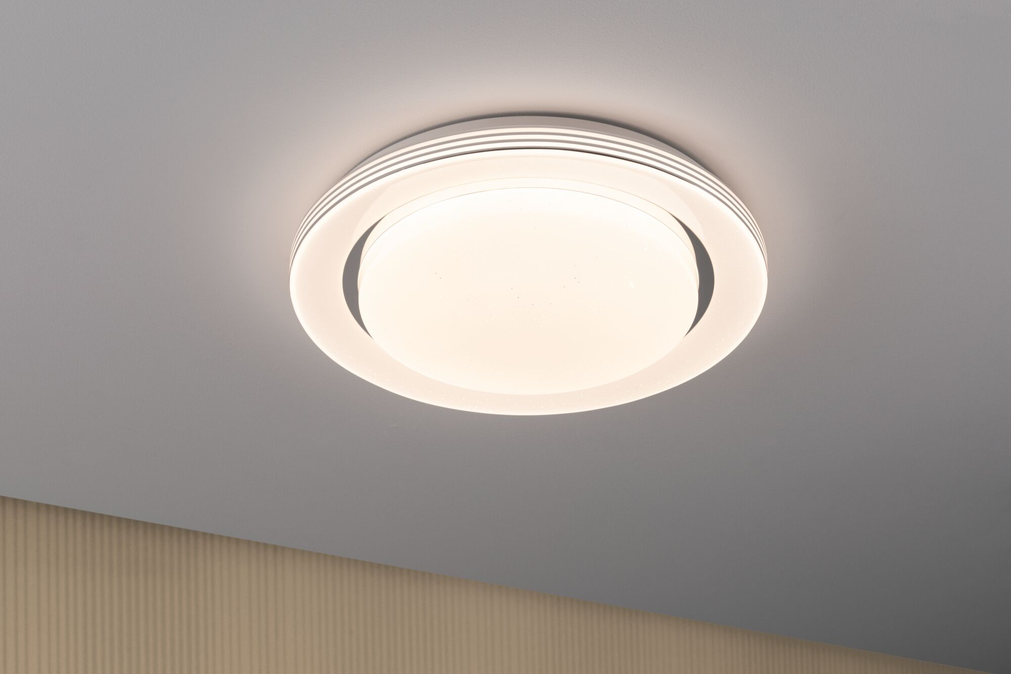 Una plafoniera bianca con diffusore rotondo illuminato e dettagli ad anello.