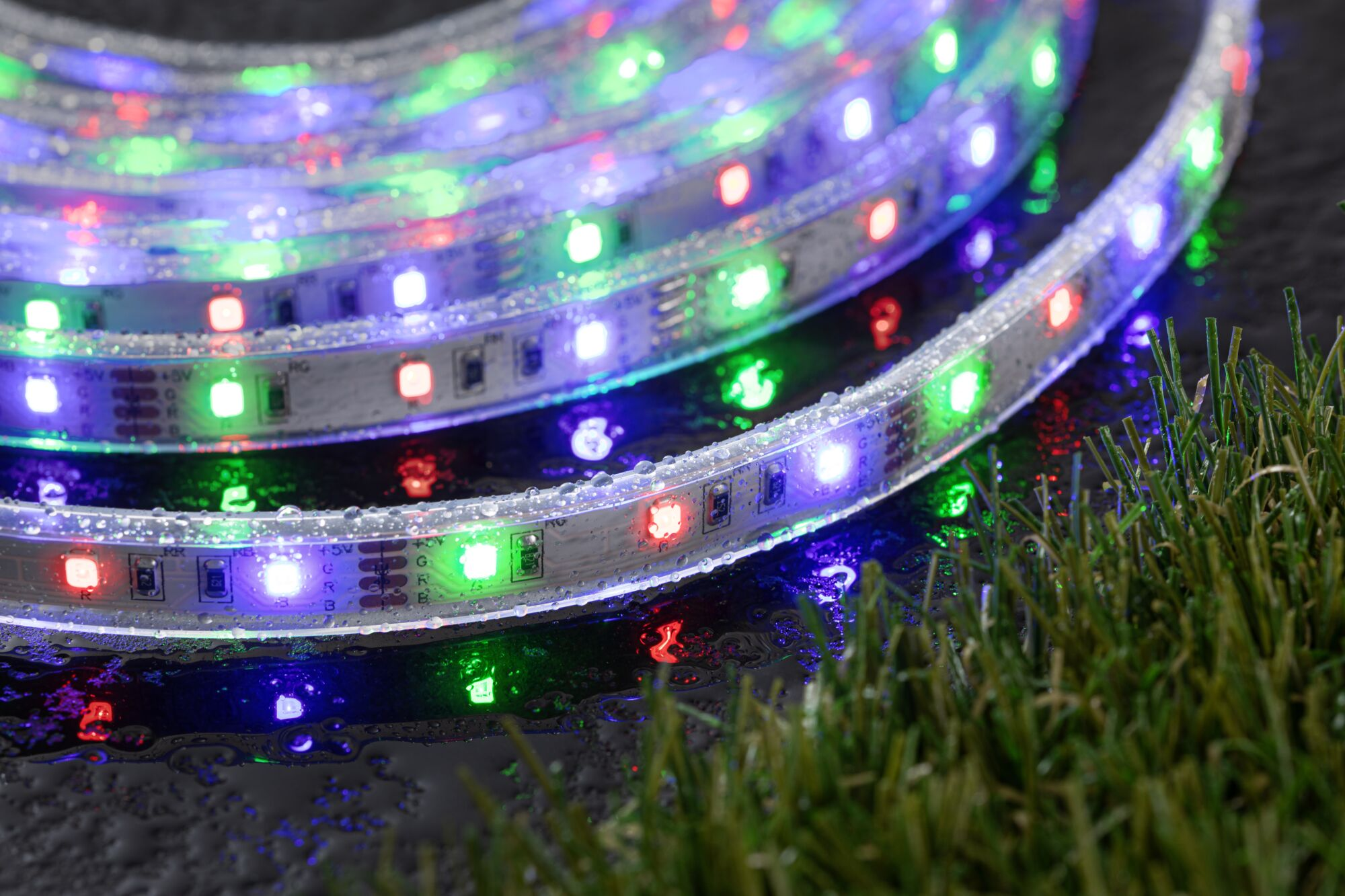 Ein LED-Streifen mit roten, grünen und blauen Lichtern liegt auf nassem Untergrund.