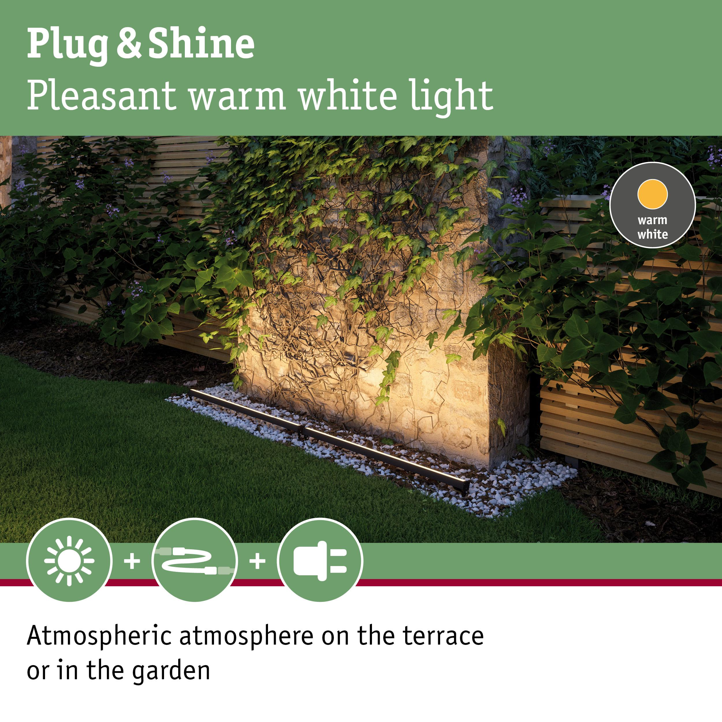 Gartenbeleuchtung mit warmweißem Licht erhellt Steinwand und Grünpflanzen.