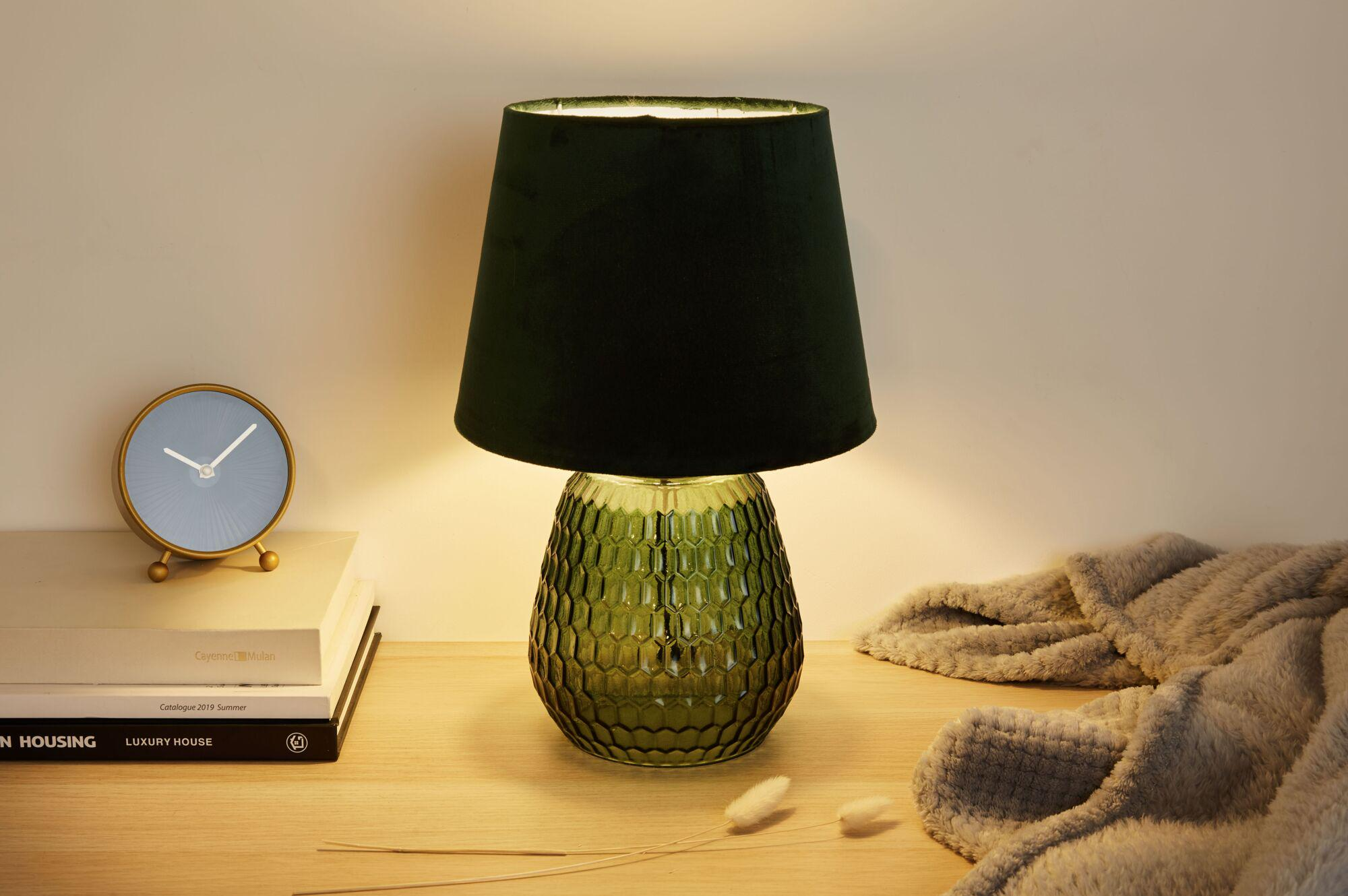 Zielona lampa stoi na drewnianym stole obok książek i koca.