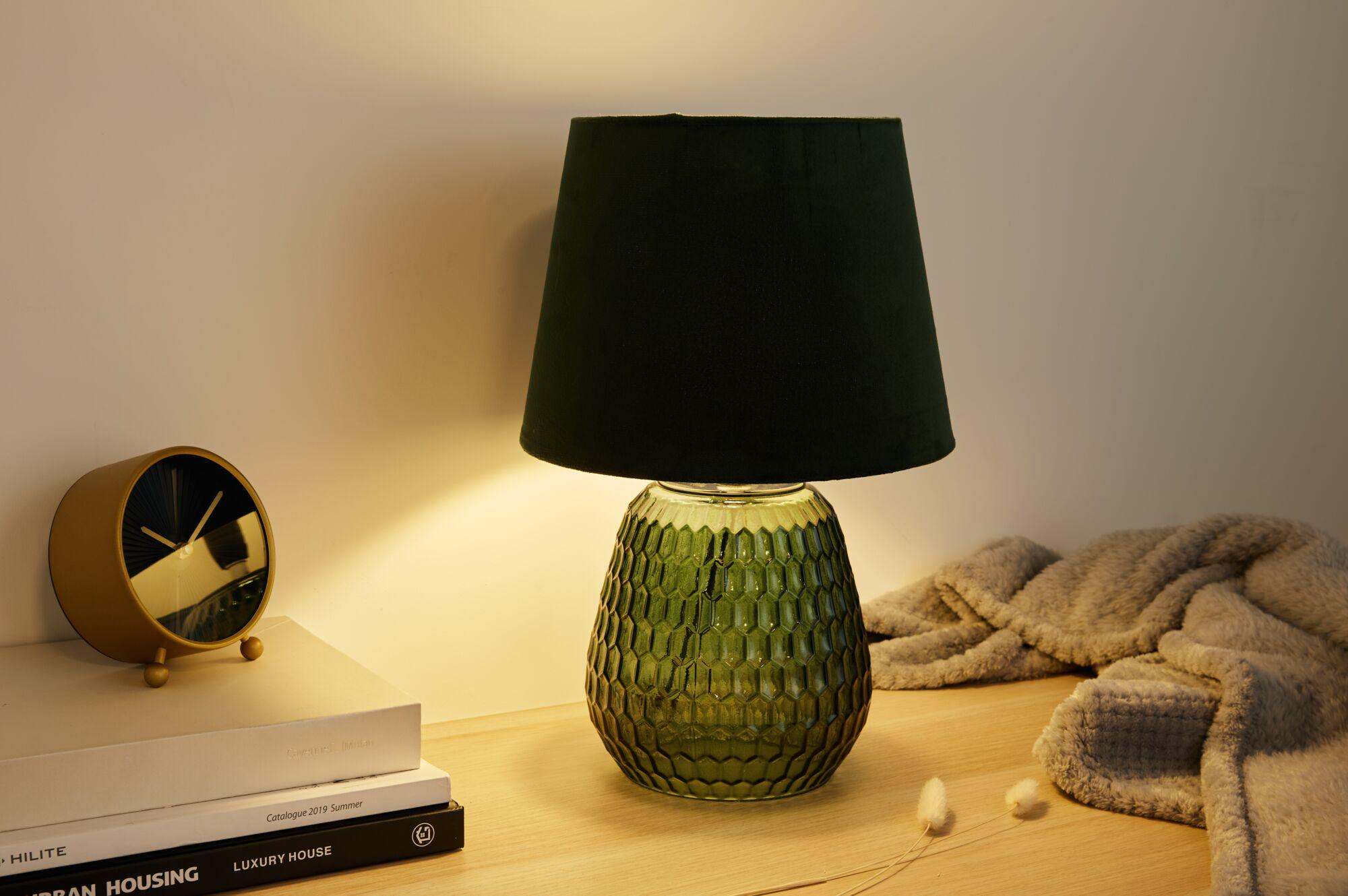 Zielona lampa z ciemnozielonym abażurem, obok zegara i książek.