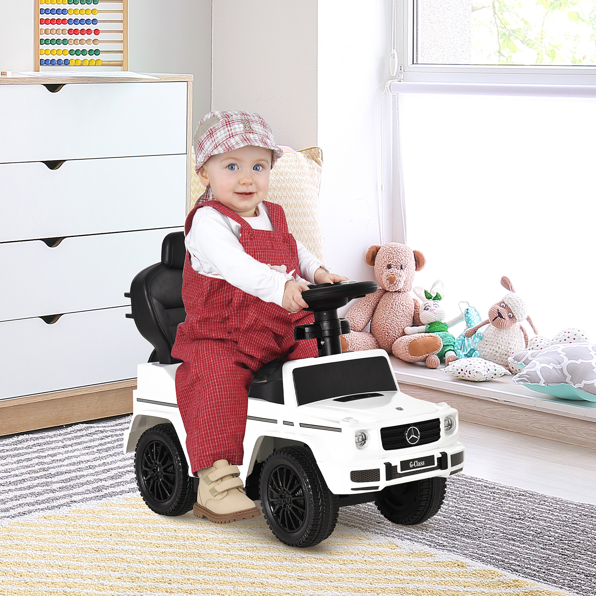 Un bebé con peto se sienta en un coche de juguete blanco.