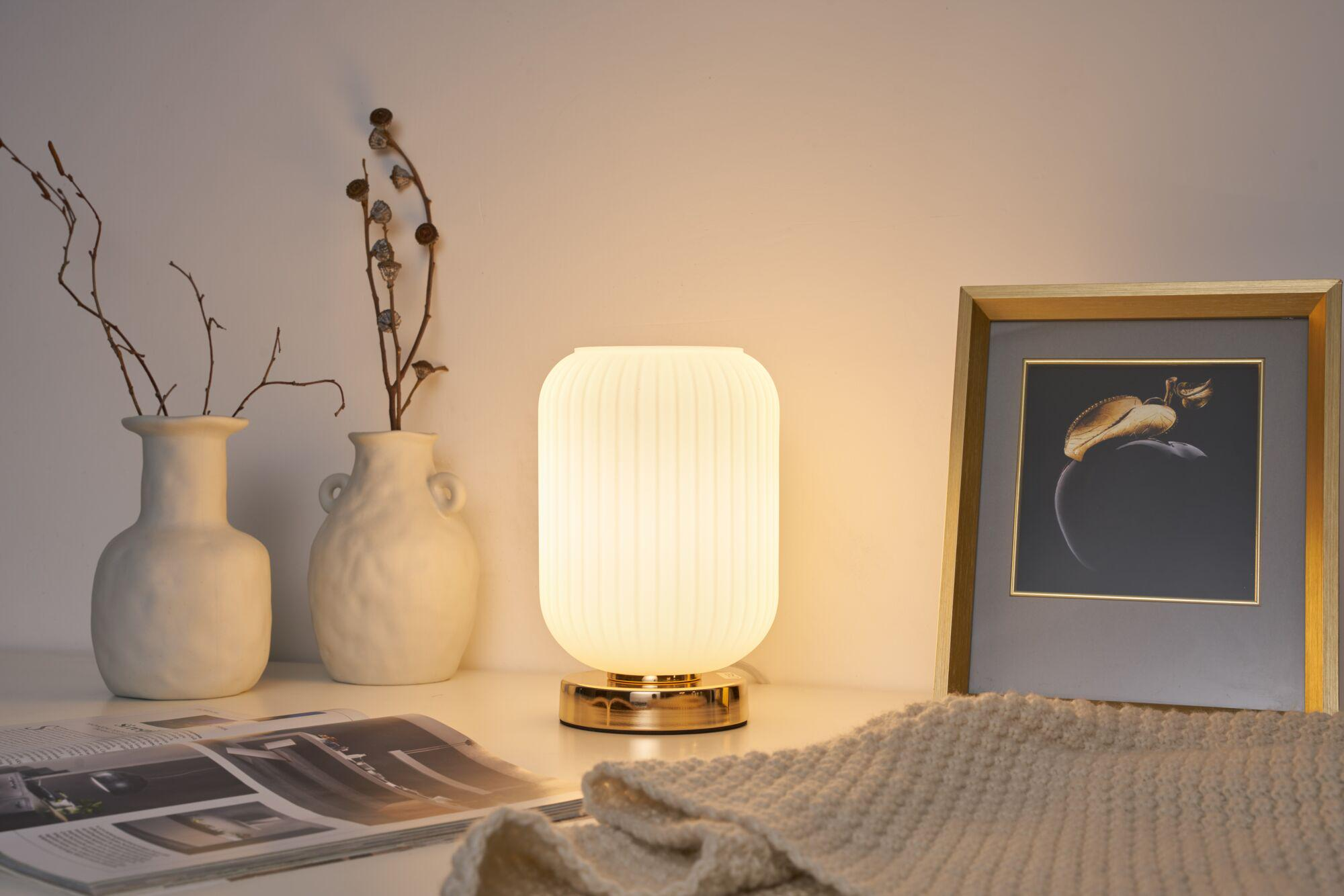 Świecąca lampa obok dwóch wazonów, obrazu i koca.