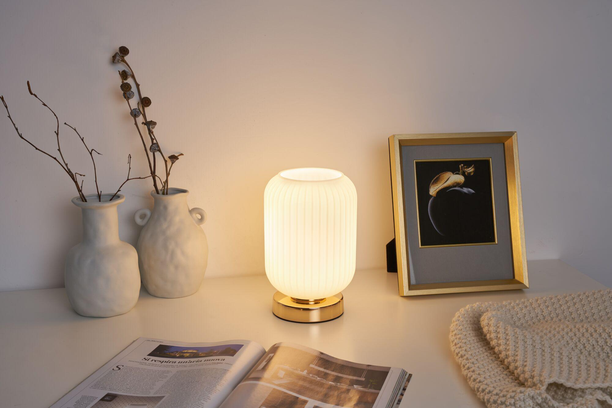 Stolik nocny z lampą, wazonem, gazetą i obrazkiem.