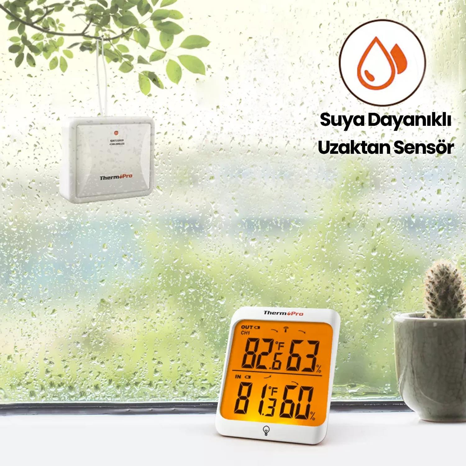 Beyaz bir termometre sensörü, yağmur damlalı bir pencerenin önündeki ağaç dalından sarkıyor.