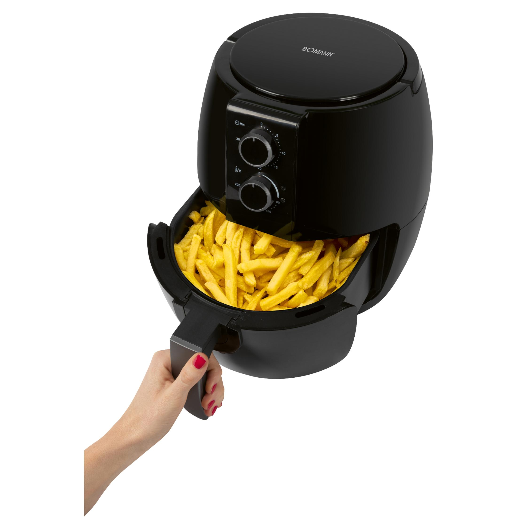 Schwarze Heißluftfritteuse mit vollem Korb Pommes Frites, die von einer Hand herausgezogen wird.