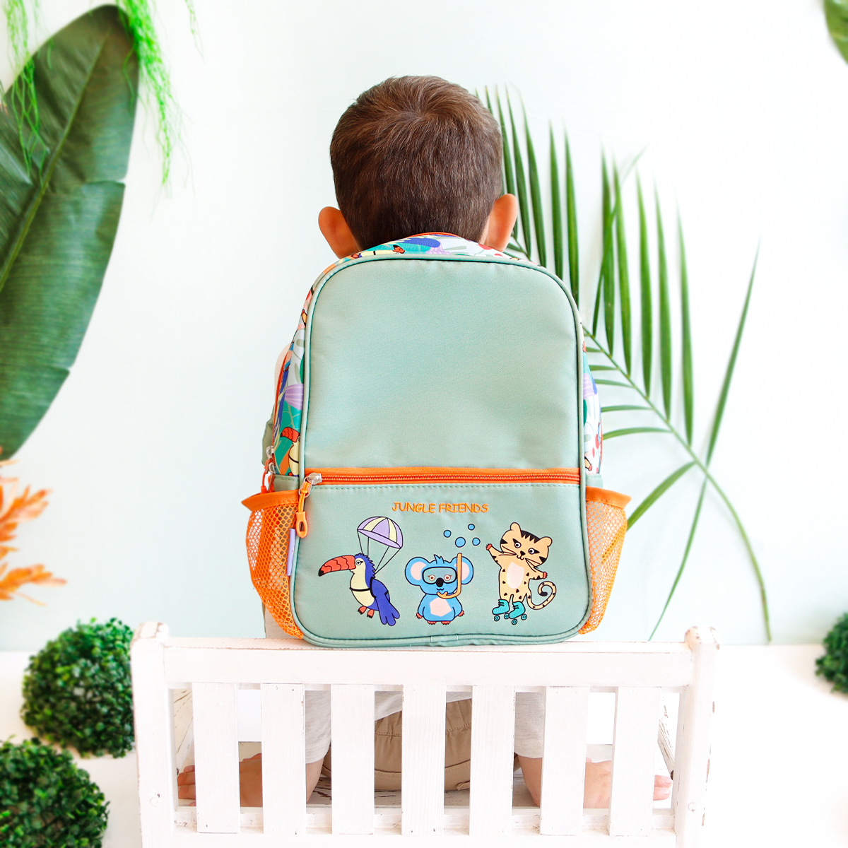 Una mochila verde claro con estampado de animales de la selva, llevada por un niño en una silla.