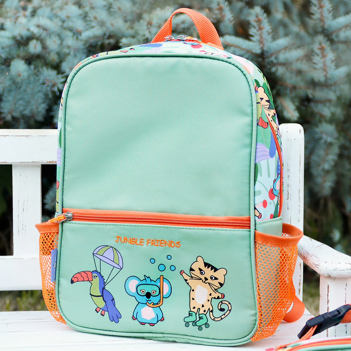 Una mochila verde claro con estampado de animales de la selva se sienta en un banco blanco.
