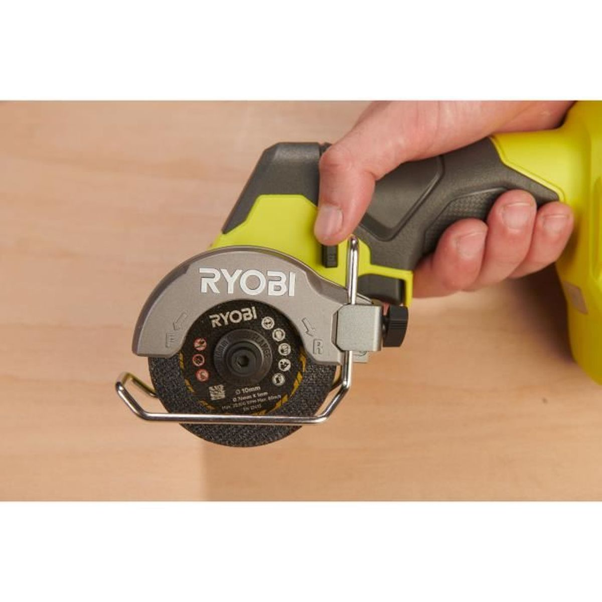 Une main tient une scie circulaire Ryobi jaune et grise avec un protecteur métallique.