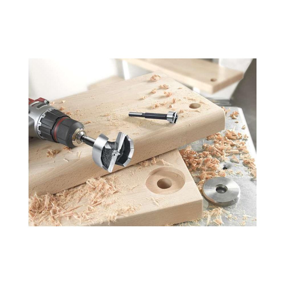 Bohrer mit Lochsäge auf Holzbrettern, Sägespäne verstreut.