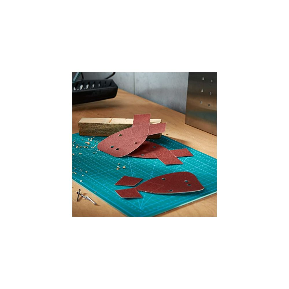 Rote Schleifpapierblätter mit Löchern liegen auf einer grünen Schneidematte.