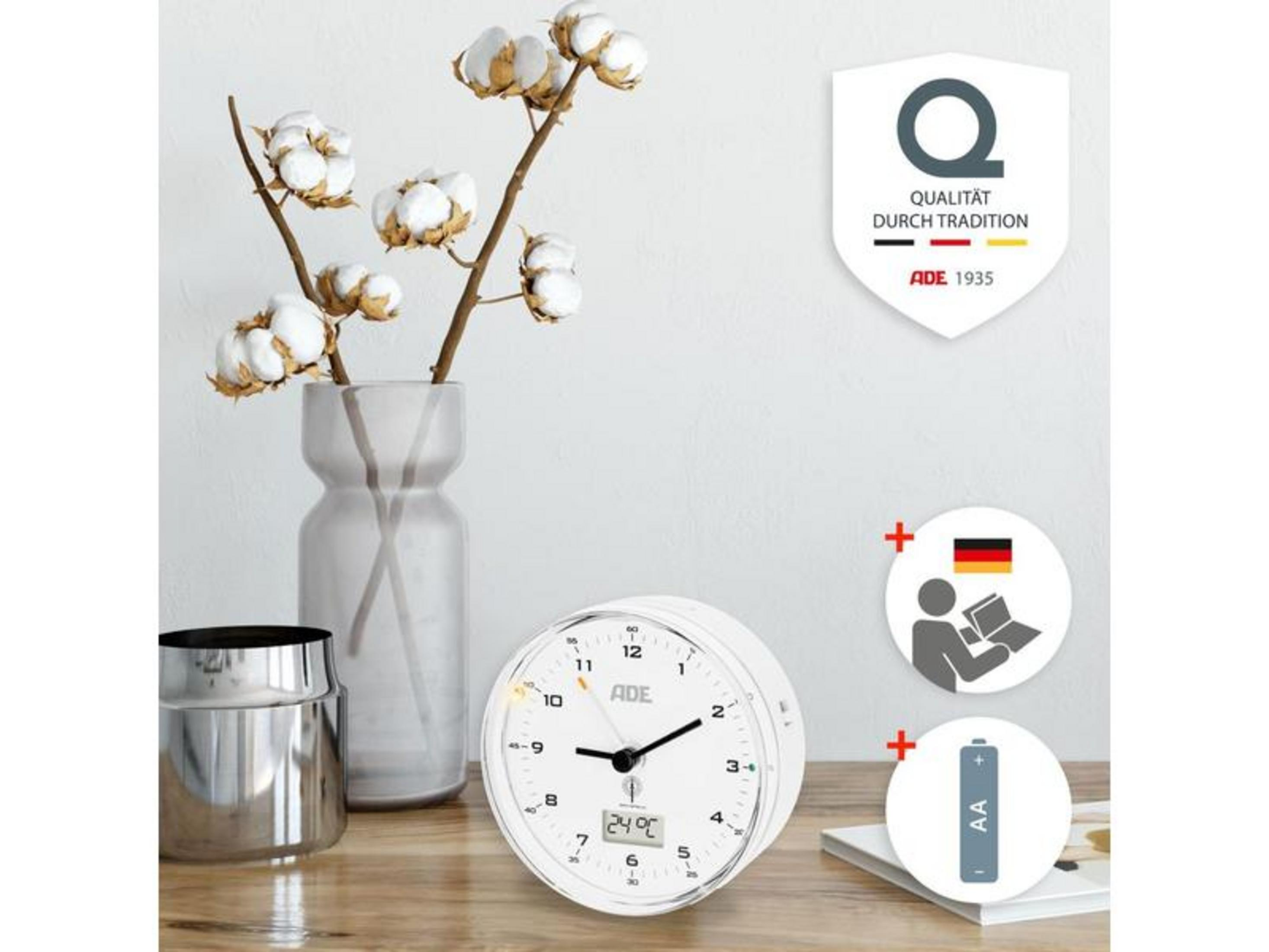 Ein weißer Wecker mit Temperaturanzeige, Baumwollzweigen in einer Vase und einem Metallbecher.